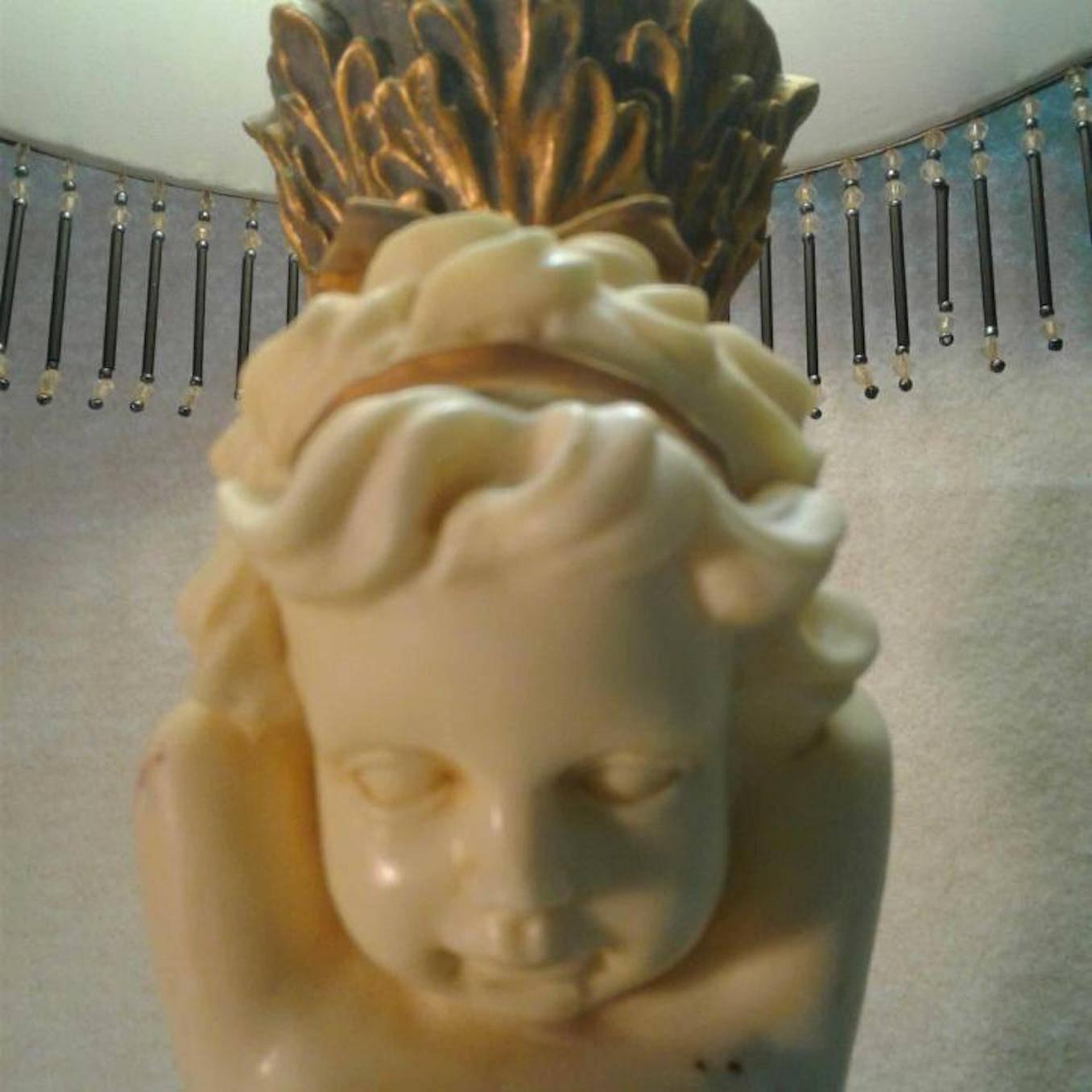 Cherub table lamp

Stamped J. Upton. Lamp with a two cherub features ornate brass colored details appears to be a made of resin. The lampshade is a gray Victorian style and has black tassels with clear Â beads.