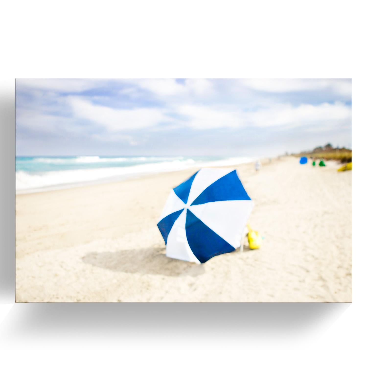 ‘Beach Series: Lone Umbrella' Mounted Plexiglass Limited Edition Photograph features a hazy beach scene in tones of blue, yellow, sand, white, and green. Inspired by nature and human connectivity, the intimacy behind her work is evident. Renowned