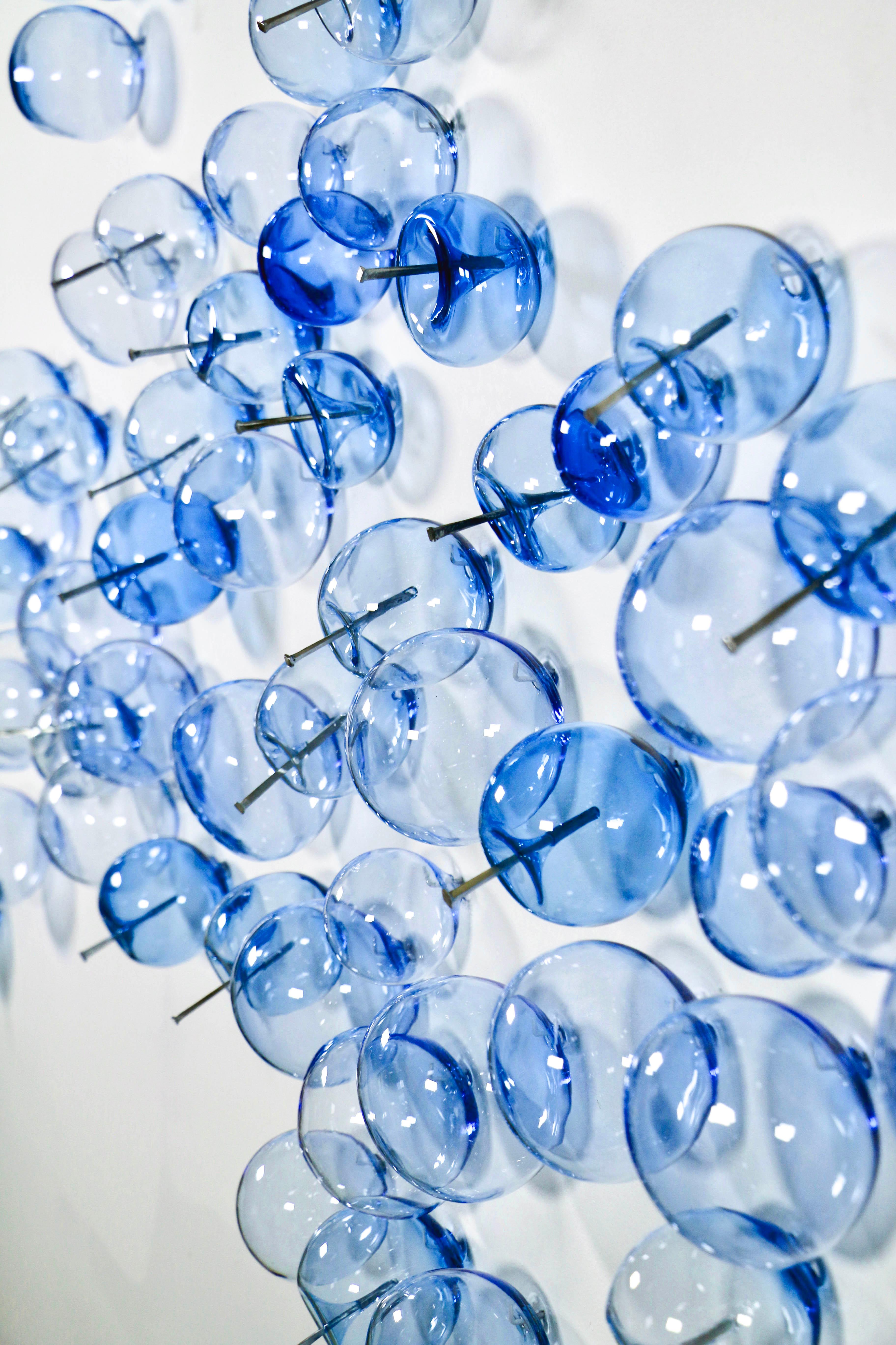 Cette sculpture murale contemporaine en verre de couleur bleu céruléen a été créée par Cheryl Wilson Smith.

Les œuvres en verre de cette artiste canadienne, d'une beauté unique, sont connues pour leur forme, leur couleur et leur texture, souvent