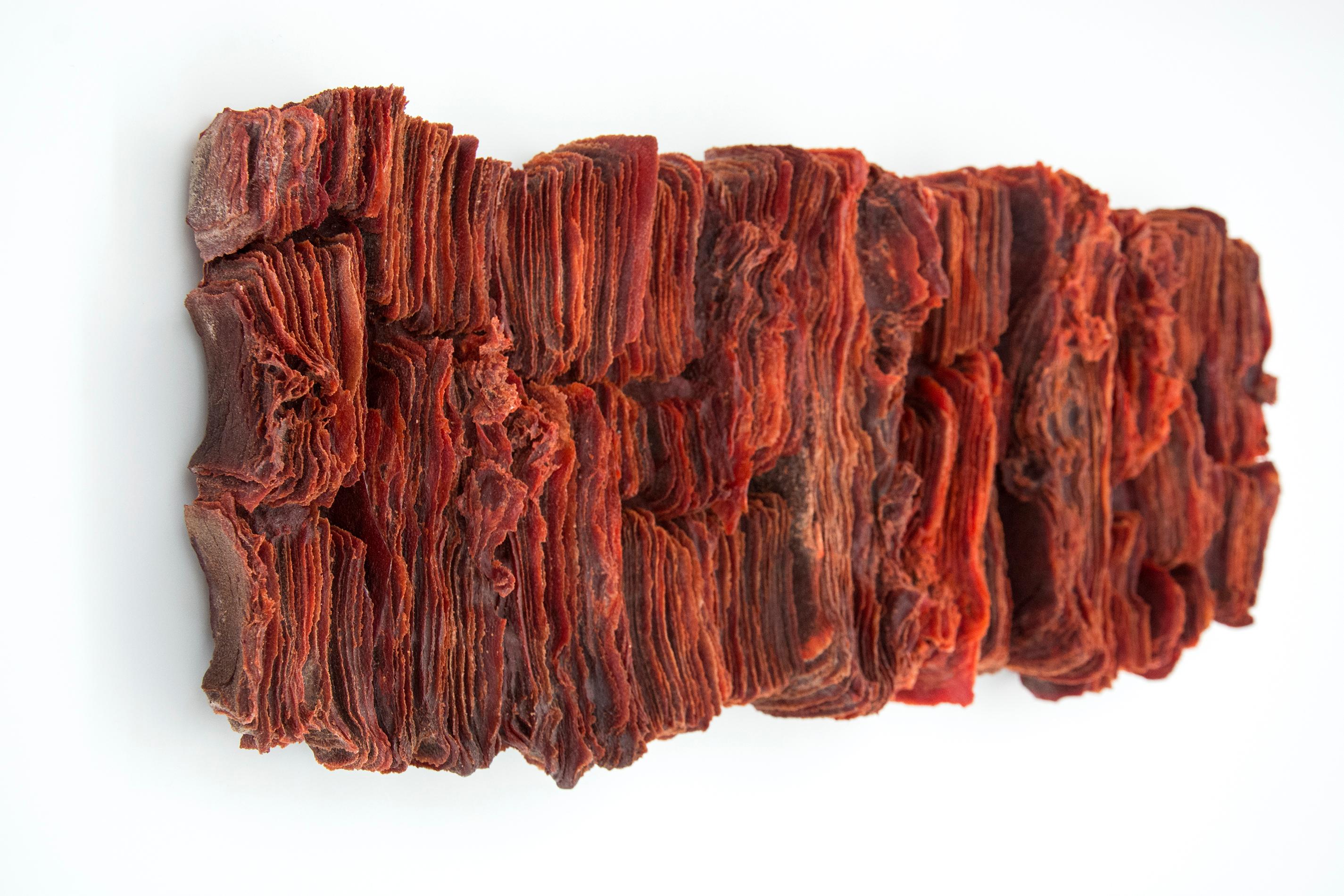 Wafers of red copper glass frit are stacked and layered in this modernist wall sculpture by Cheryl Wilson Smith. Wilson Smith's work is created by forming minute glass particles, known as frit, into paper thin pieces from which she creates her