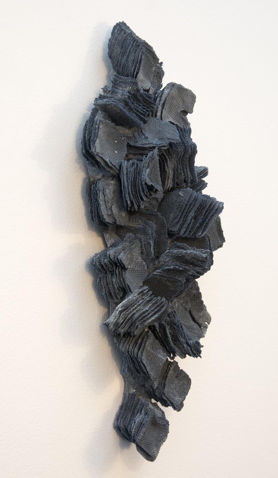 Wafer thin layers of textured indigo blue glass frit squares are stacked on the horizonal and vertical to form a dynamic diamond-shaped wall relief by Cheryl Wilson Smith. Wilson-Smith has lived in northern Ontario for many years 