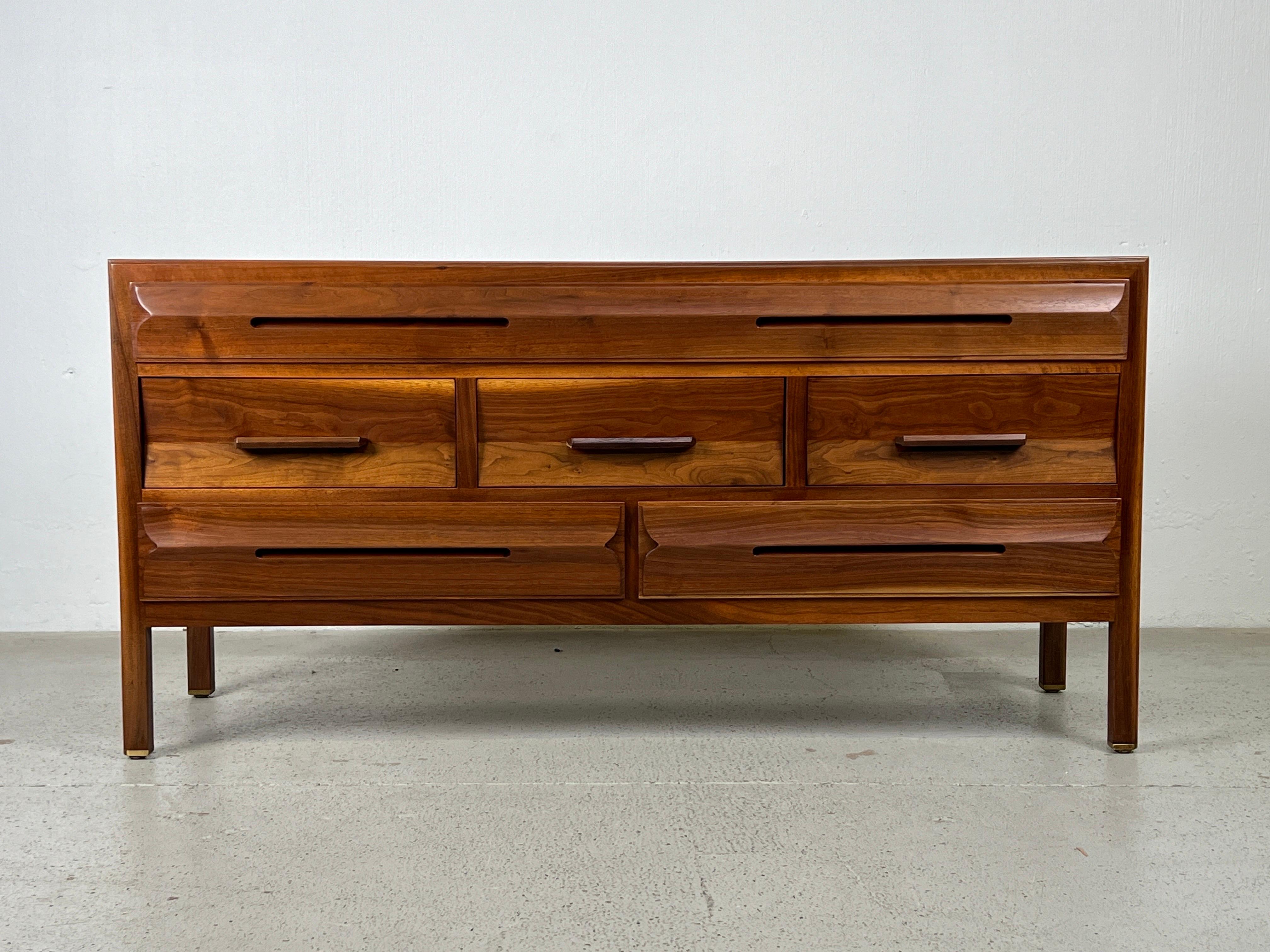 A walnut dresser with sculpted drawer fronts and rosewood handles and brass feet. Designed by Edward Wormley for Dunbar.