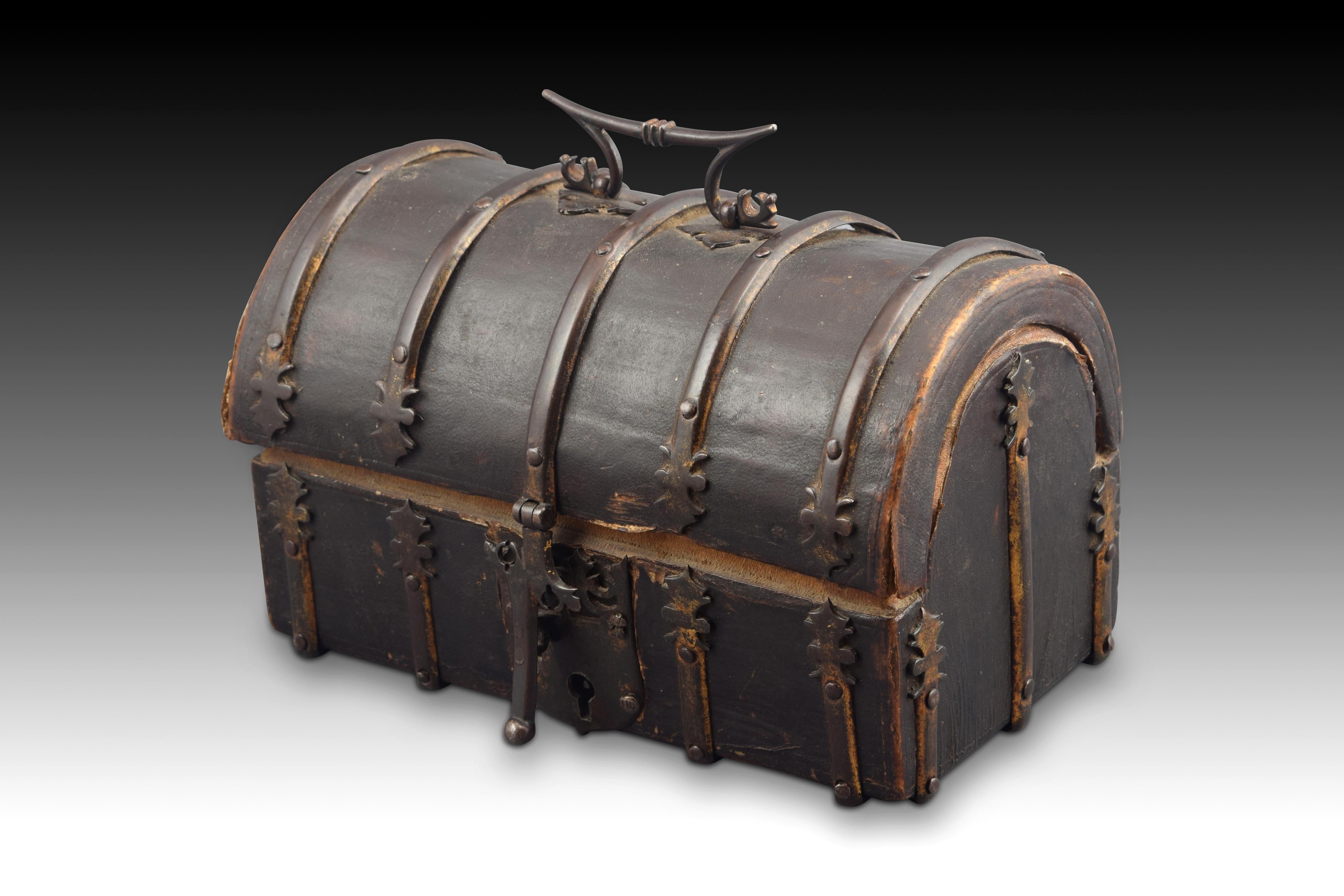 Rectangular body casket with semicircular lid made of carved wood and covered with a worked leather that has been reinforced with a series of forged iron fittings, material in which the handle is also made on the lid and a bolt on the front with
