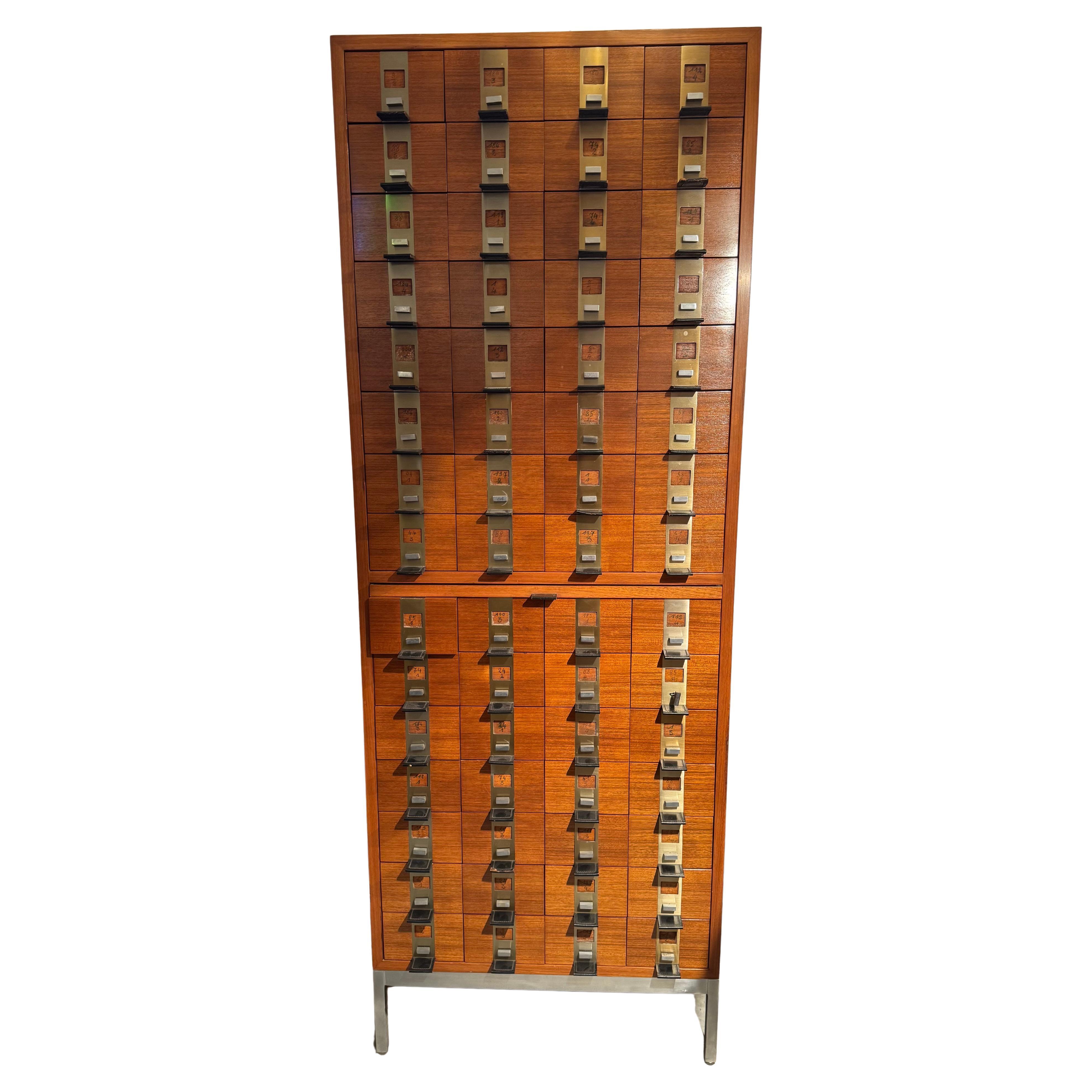 This storage cabinet features 60 drawers and a pull-out worktop in the center of the unit, hand-crafted from solid wood with walnut fronts and leather handles and a stainless steel base. A beautiful drawer front with leather handles and chrome