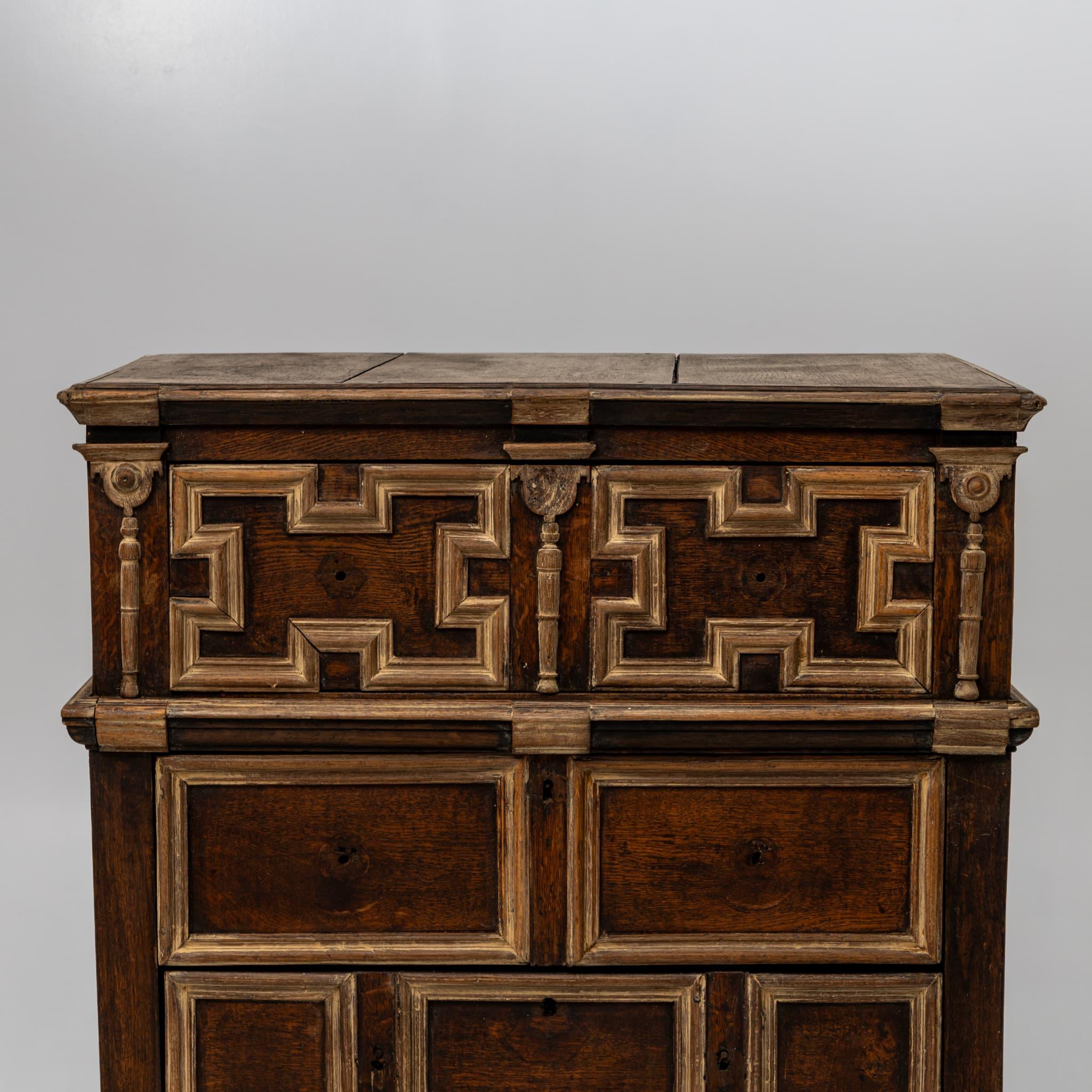English chest of drawers with four drawers and paneled fronts and sides. The surfaces are structured with profiled moldings that stand out due to the limed finish, lending the piece a striking sense of depth and character.