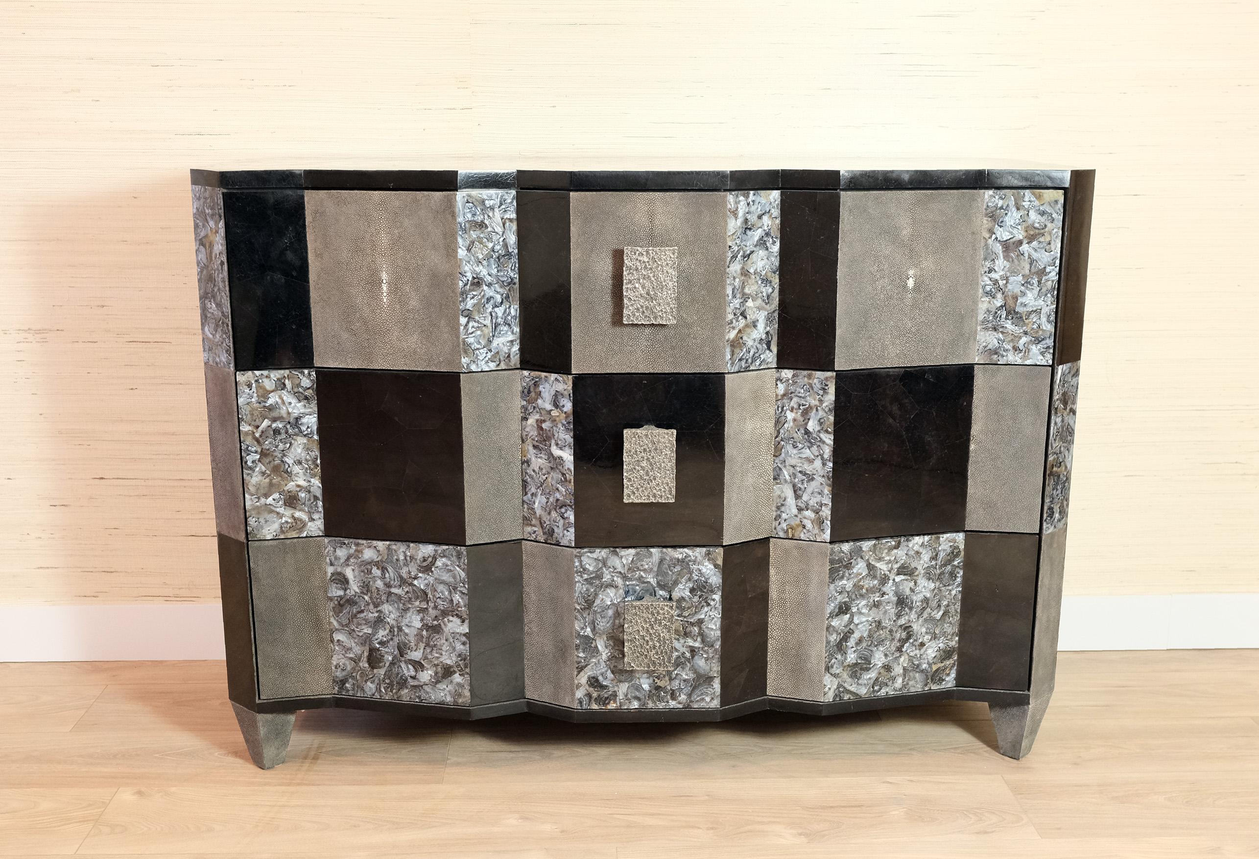 Il comò Accordeon è uno splendido pezzo futurista realizzato in intarsio di conchiglie nere e grigie lucidate con dettagli in zigrino. Ha tre cassetti.
Le maniglie sono realizzate in ottone fuso a cera persa con una patina di nichel