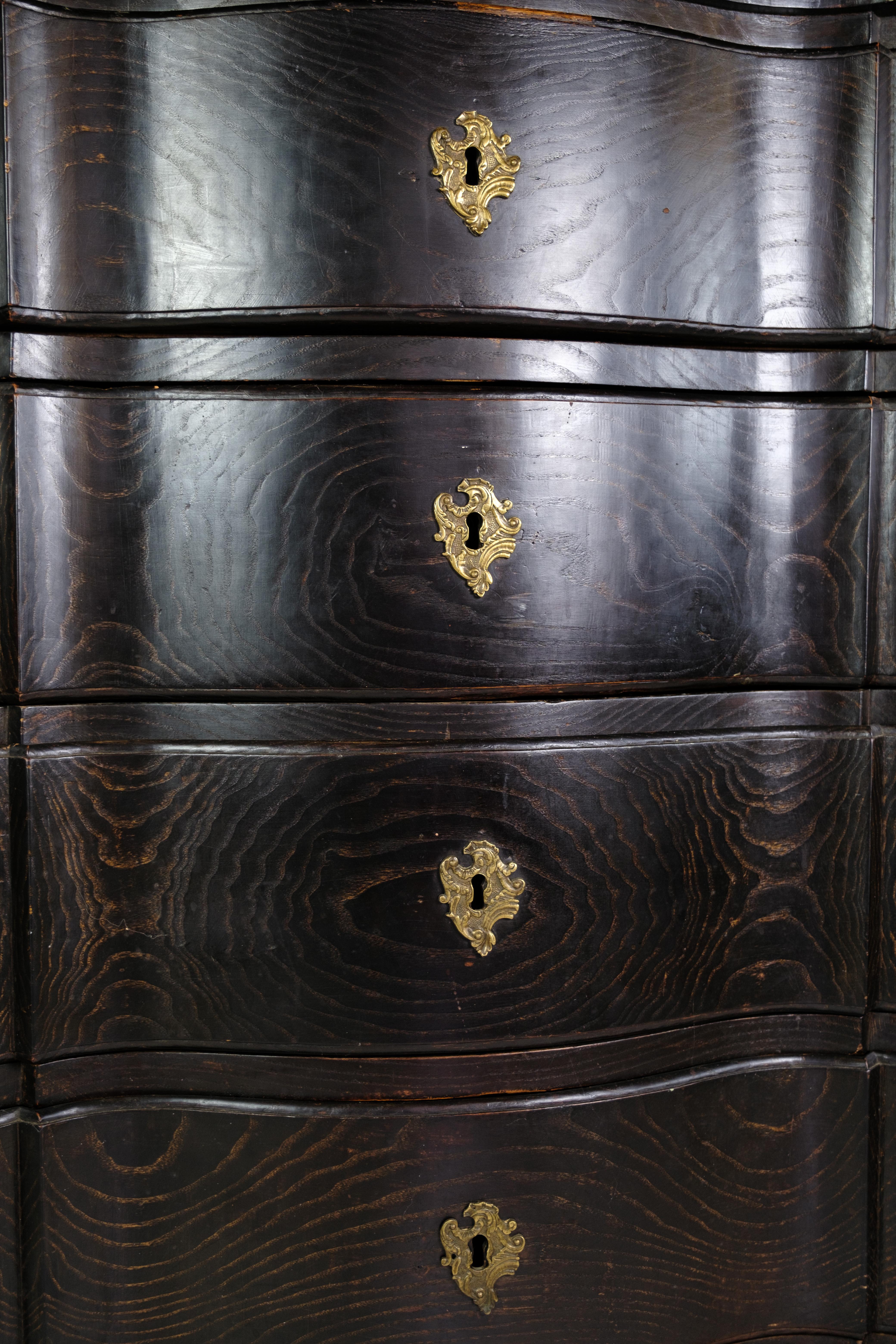 Chest of drawers in stained oak with brass fittings decorated with wood carvings from the period around the 19th century. Has a total of 4 drawers and key included.
Dimensions in cm: H:111 W:120 D:60