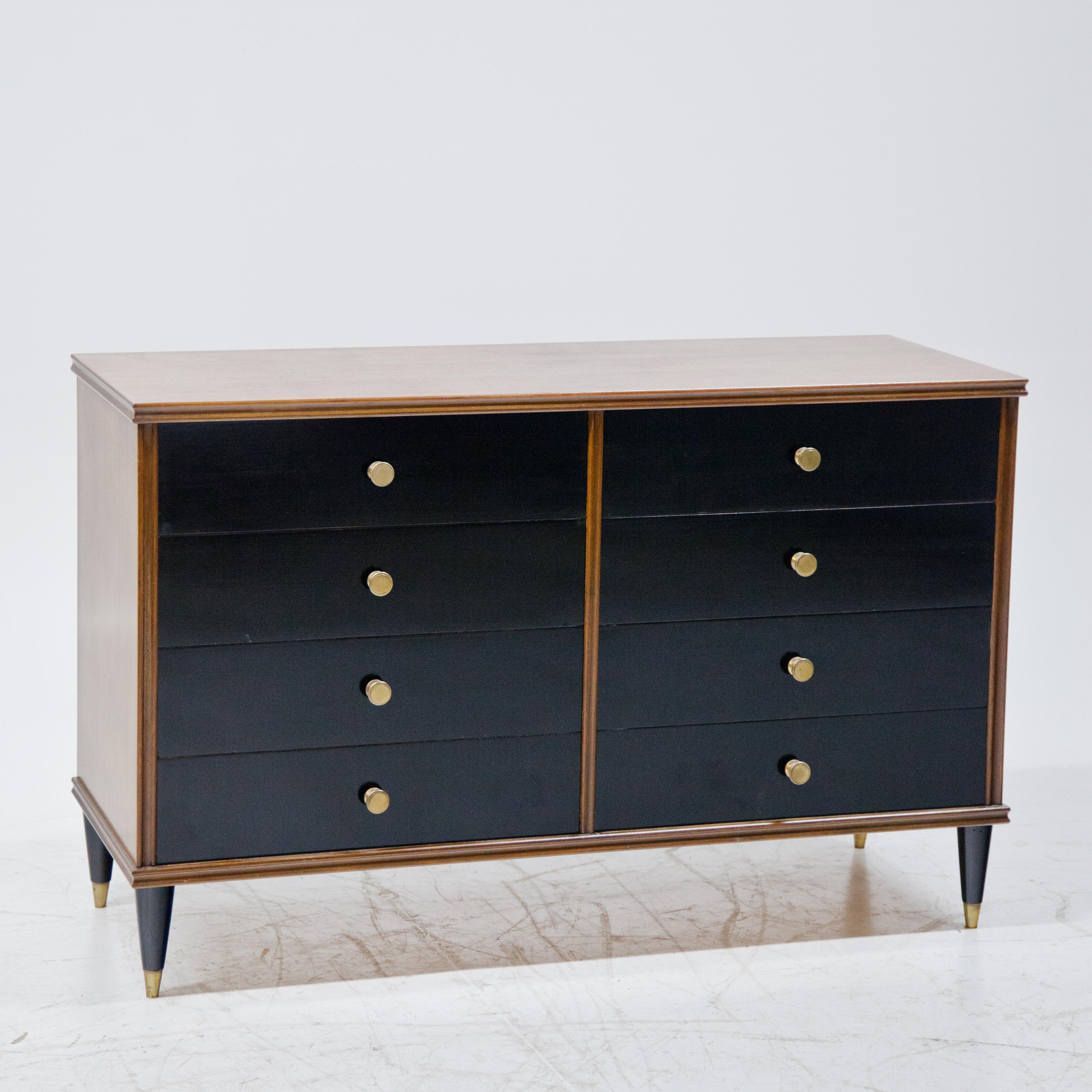 Italian midcentury chest of drawers on conical black feet with brass sabots. The straight-line body with profiled edges and eight drawers with round pull handles and blackened front.