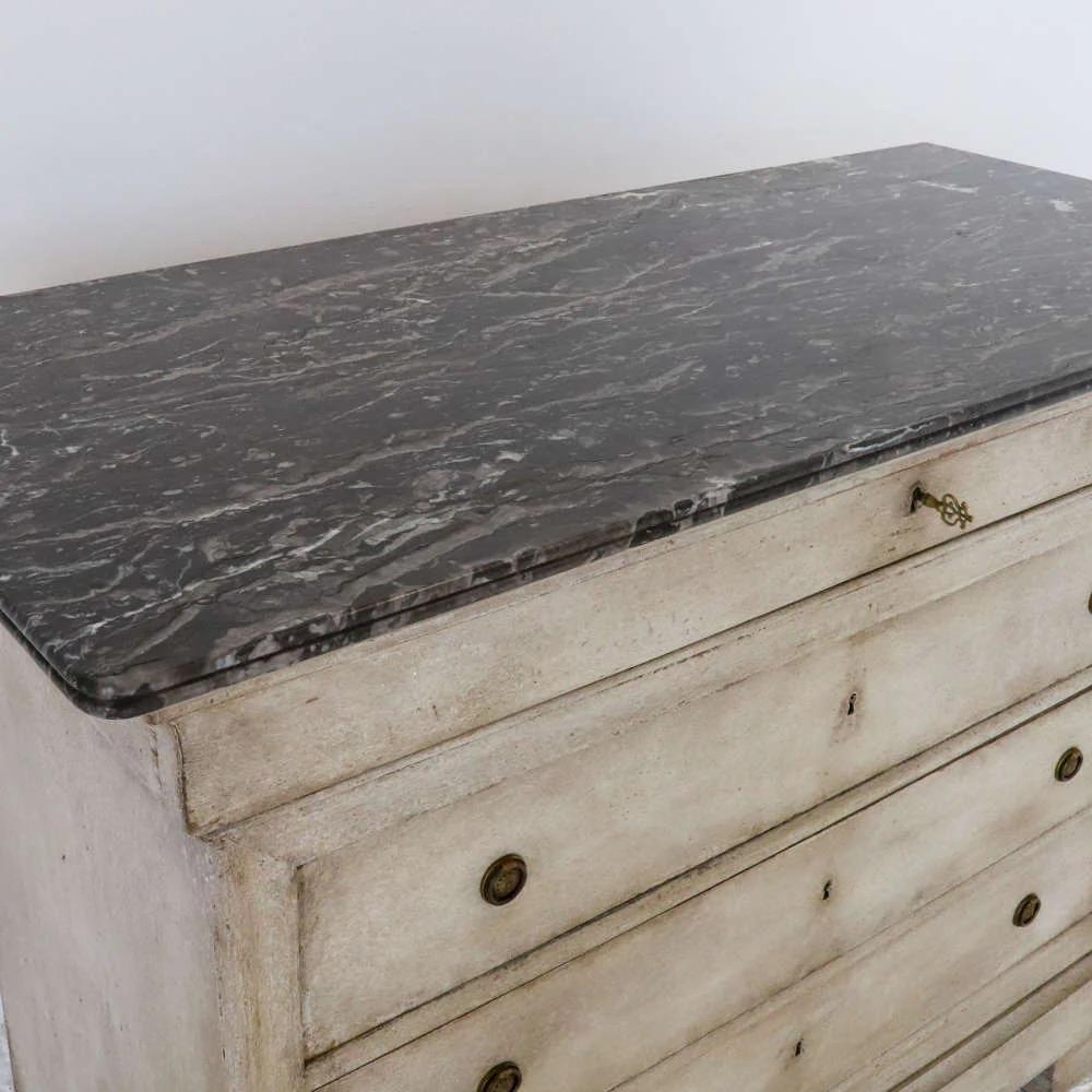 Cassettiera francese del XIX secolo dipinta di bianco con piano in marmo originale e finitura elegantemente invecchiata. Questo pezzo classico e di transizione vanta un ampio spazio di archiviazione con tre cassetti spaziosi, ognuno dei quali è