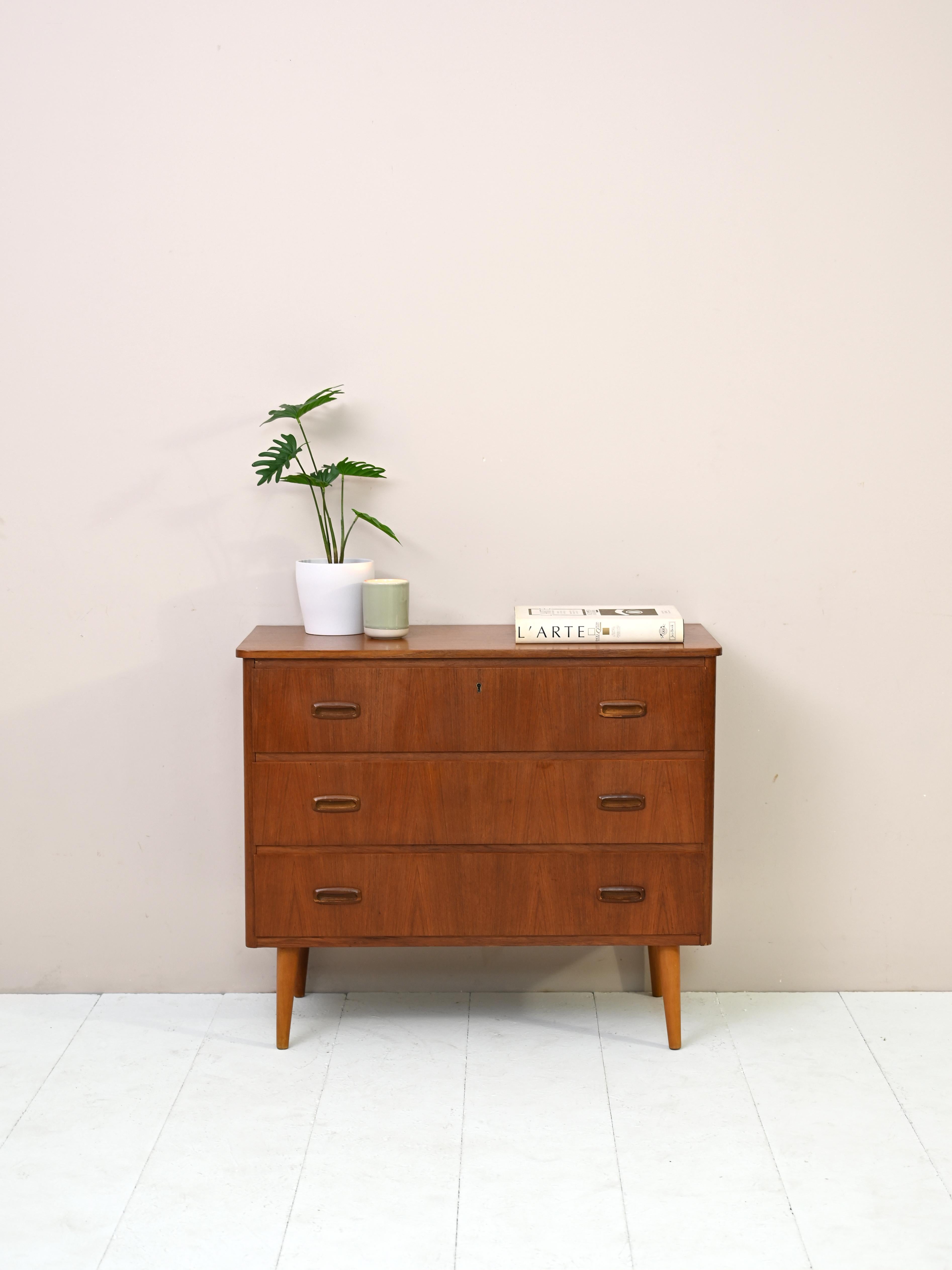 Furniture of Nordic manufacture from the 1960s.
This small chest of drawers features three drawers, the first of which has a lock.
The carved wooden handle is typical of Scandinavian design of the time.
The light oak conical legs give a modern