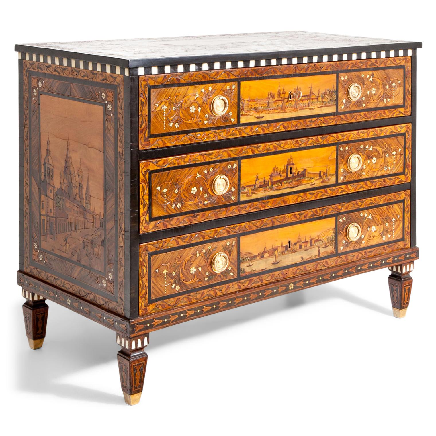 Three-drawered chest of drawers, standing on tapered legs with rich marquetries in different, partly colored wood inlays. The chests shows different views of Moscow in the 18th century: At the top is a depiction of the Red Square, the right side