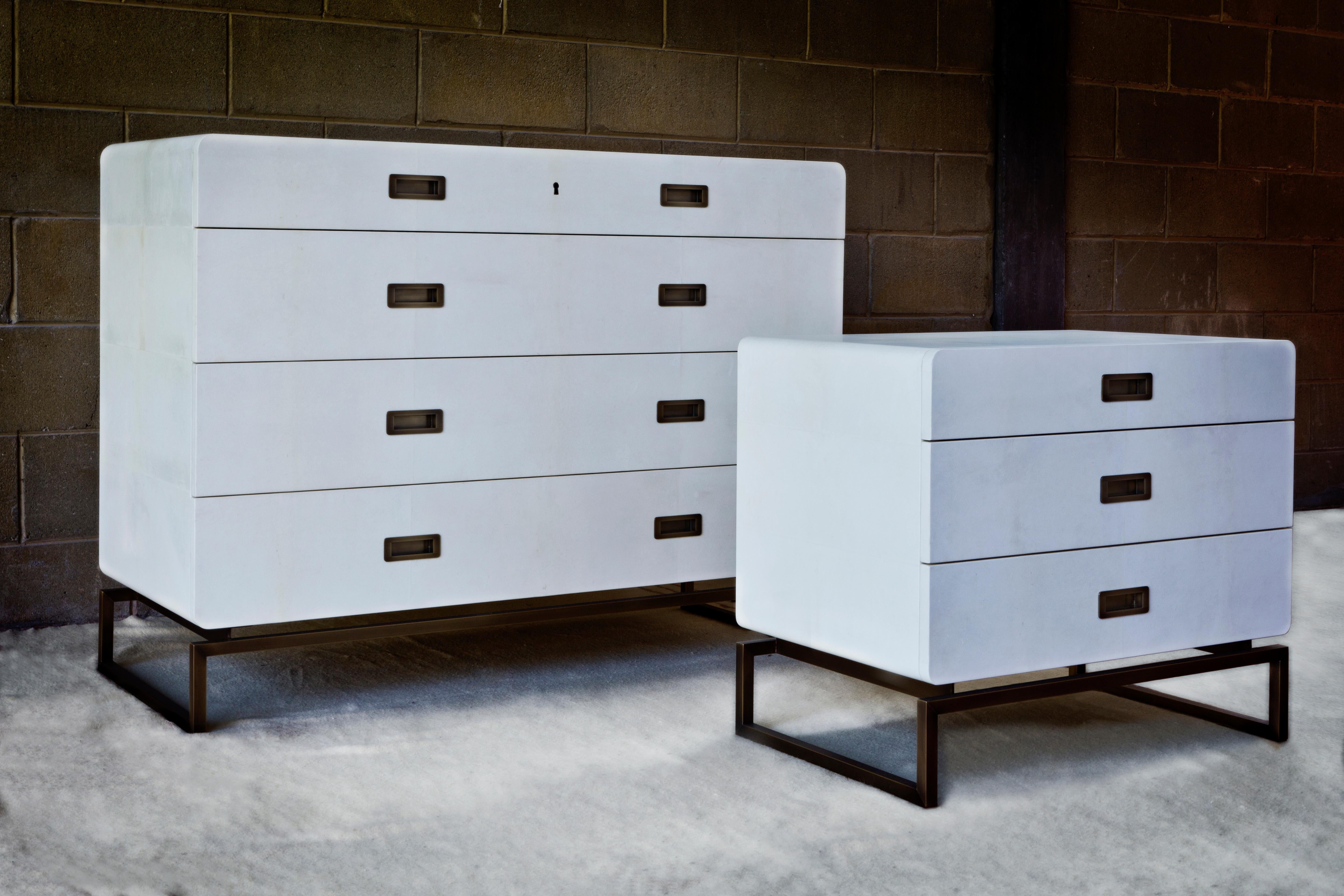 A set made up of a chest of drawers and a bedside cabinet inspired by travel trunks. The drawer element has clearly rounded corners and compact proportions, and rests on a structure of metal runners in bronze finish.

The clean lines and the