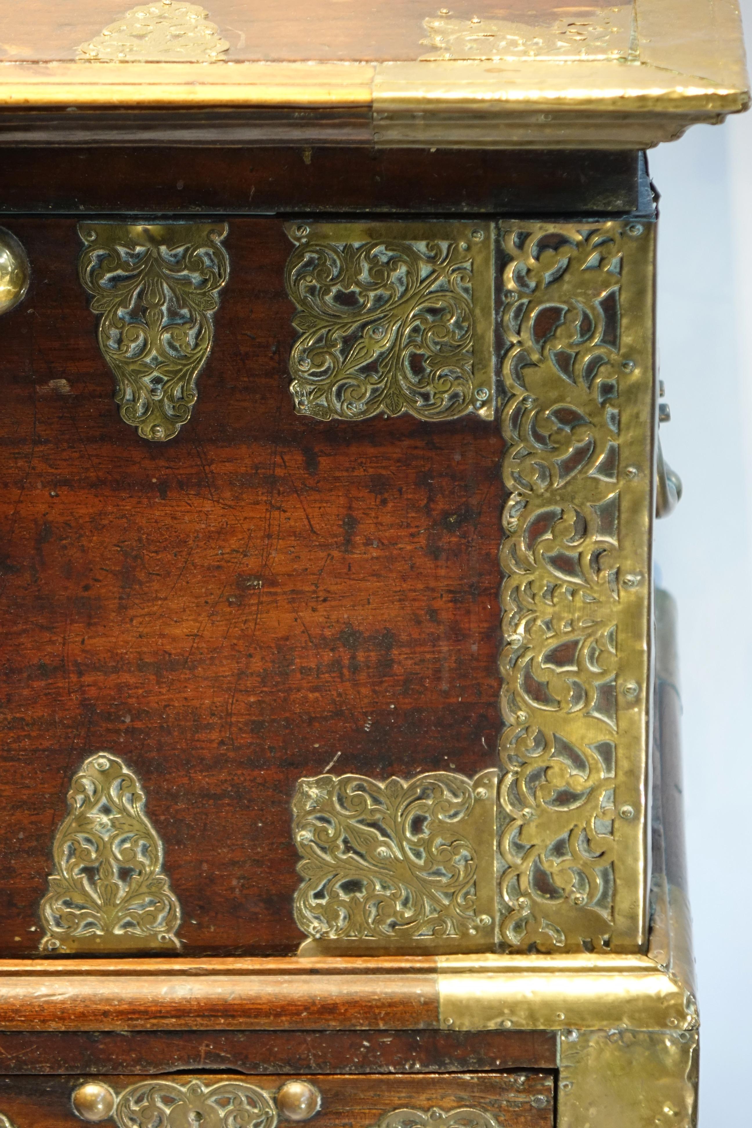 Teak wood chest with rich gilt copper applications of decorative scrolls and foliage, and probably two drooping tulips for the decoration in the center of the work top.
Handles for the drawers and carrying handles, as well as the key, are in