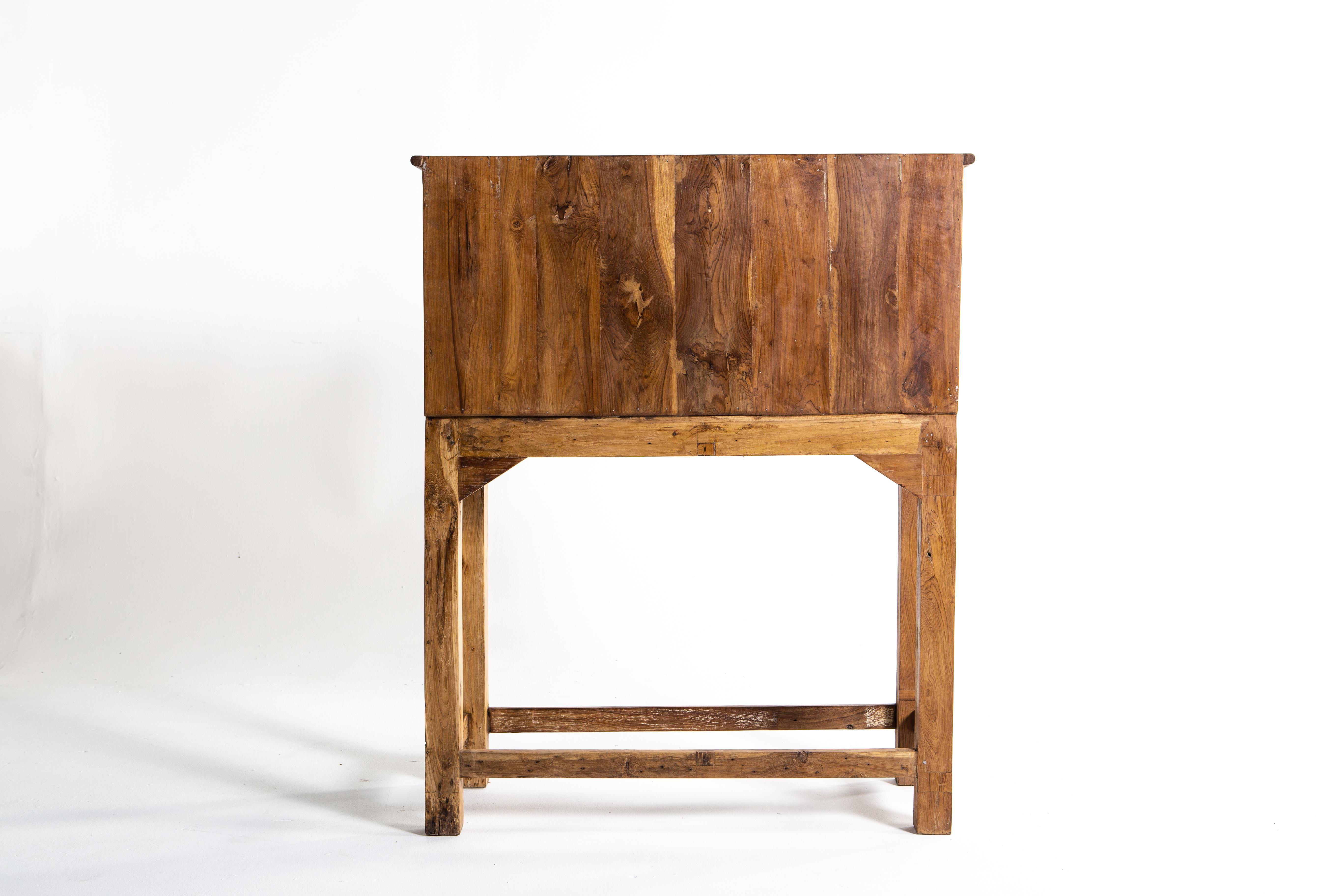 This chest features 20 drawers reminiscent of a library card catalog and two retractable shelves. Made of teak wood, the piece has a lovely golden hue and visible grain. At approximately three feet in height, the chest is functional and a lovely