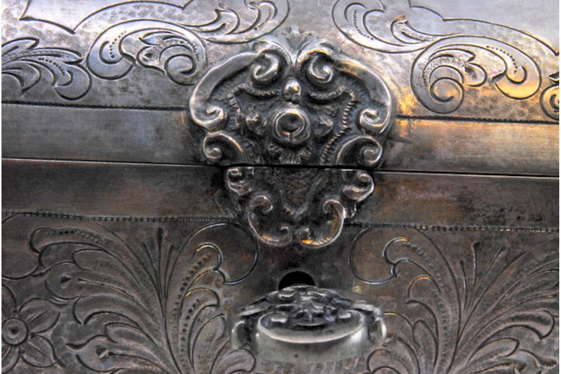 Description: Silver jewelry box in the shape of a chest with engraved plant motifs, velvety interior and key. Metal: Silver. Origin: Portuguese. Mark: standing eagle. Weight: 518.99 grams. Dimensions: 14.5x8.3cm. Content: 833/1000. Assay Mark: Yes,