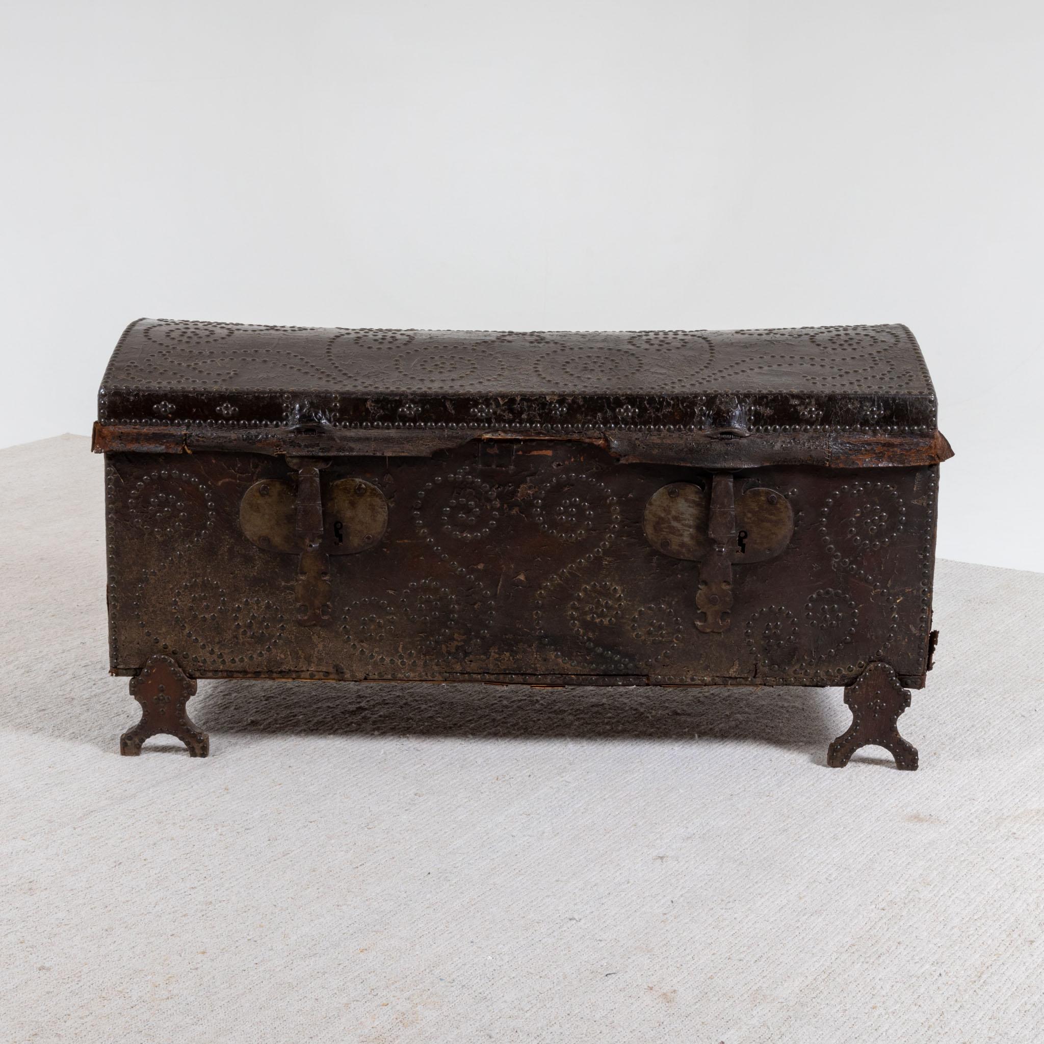 Elongated chest with a domed lid and iron fittings. The wooden chest is covered with dark brown leather and decorated with rivets. The chest stands on forked legs and is lined with fabric inside.