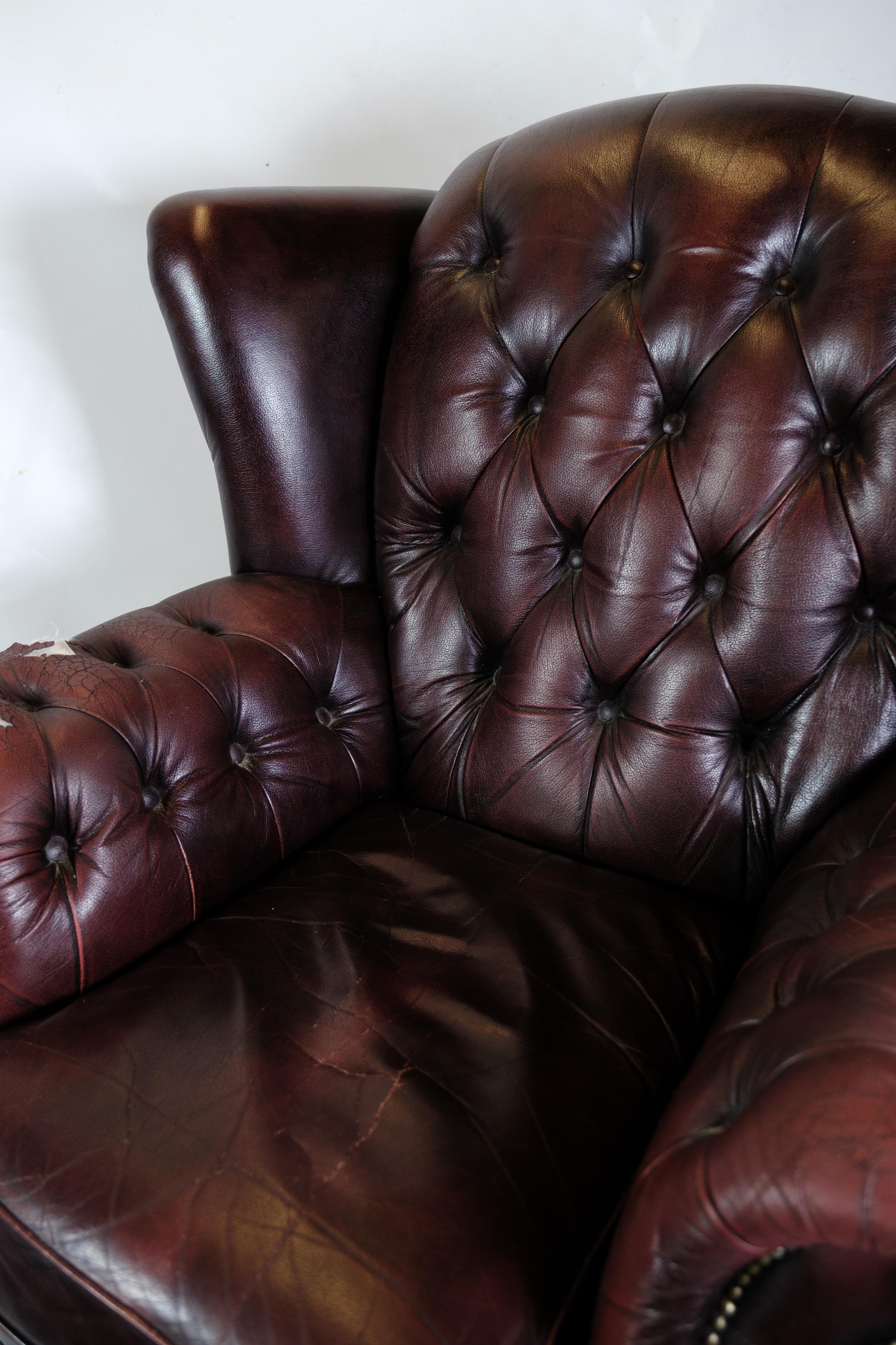 Dieser Chesterfield-Sessel mit passendem Hocker ist ein klassischer Vertreter von zeitloser Eleganz und Komfort. Mit ihren schwarz lackierten Holzbeinen und der schönen Polsterung aus genopptem Leder strahlt diese Garnitur sowohl Luxus als auch