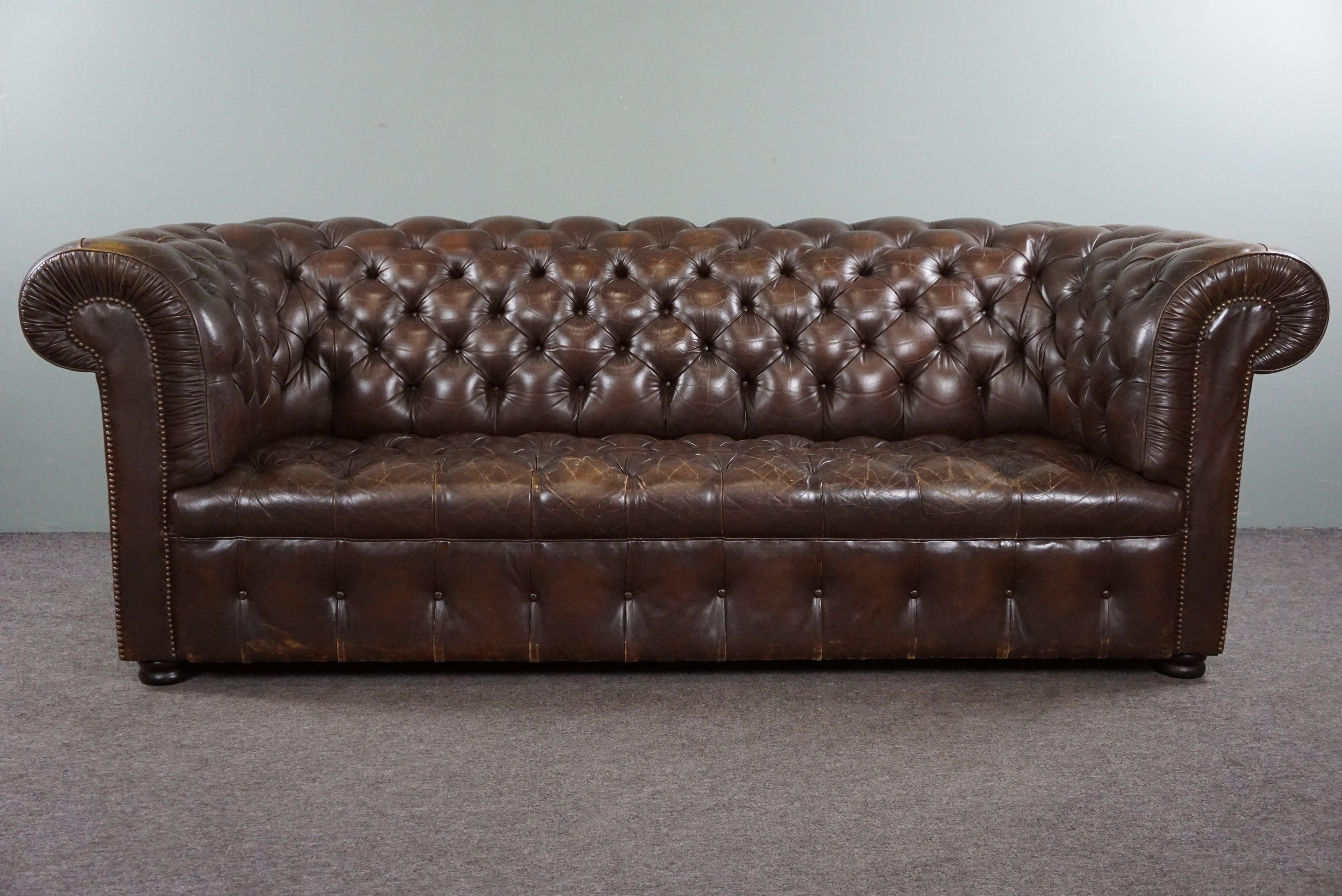 Offered is this wonderfully seated patinated antique cowhide 3-seater Chesterfield sofa with an amazing appearance due to its patina.

This Chesterfield sofa has a beautiful padded seat and a beautiful deep color. Anyone who takes this unique