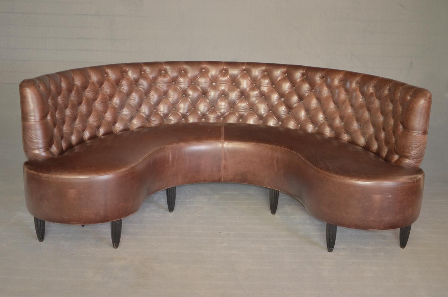 Chesterfield sofa in the shape of a dark brown English-style horseshoe dating back to 1920. The sofa features a quilted backrest typical of the Chesterfield while the back part appears to be in lateral studded velvet.
