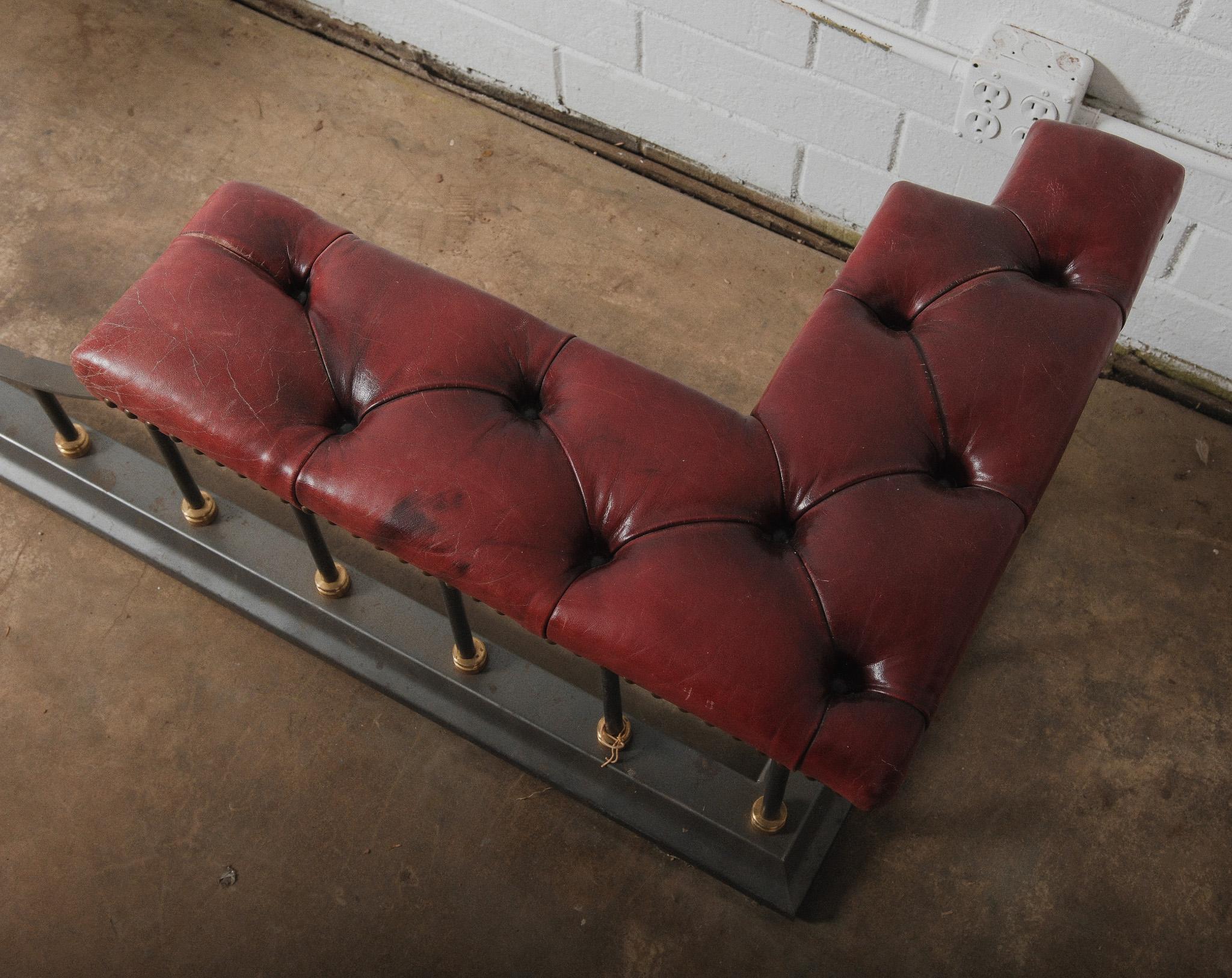Esta majestuosa defensa de palo de chimenea de estilo victoriano de mediados del siglo XX presenta asientos de cuero Chesterfield rojo burdeos abotonados en ambos extremos, sostenidos por una robusta base de hierro forjado con collares de latón