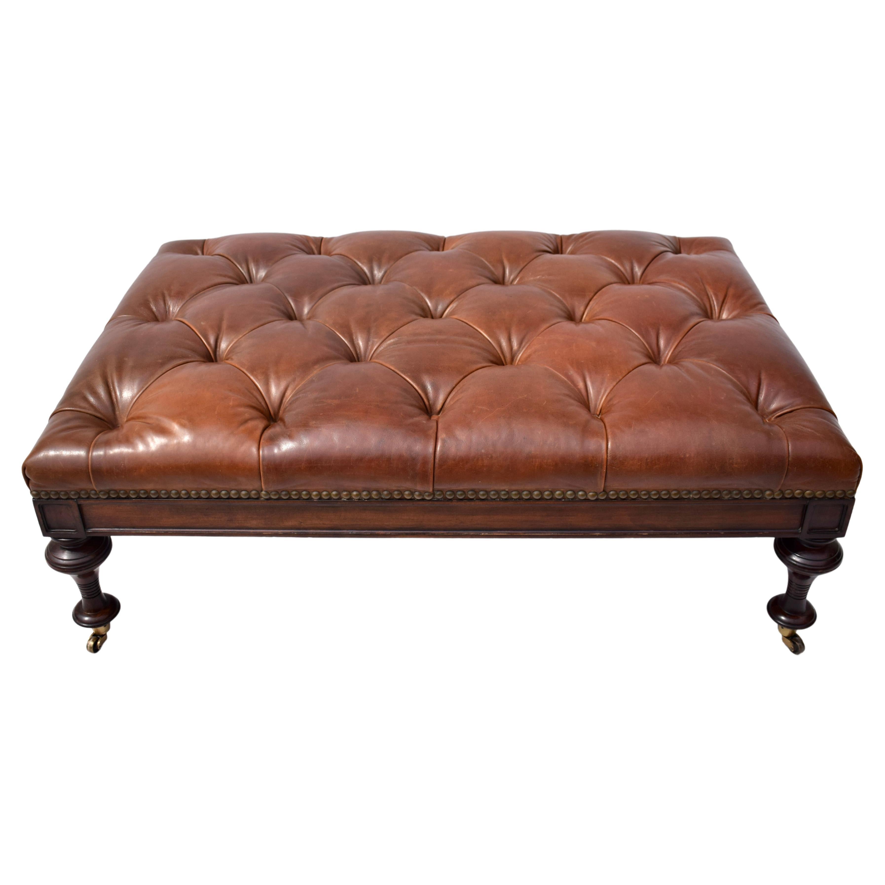 English Chesterfield Aniline leather tufted ottoman by Drexel Heritage featuring brass tack detailing with elegant turned legs on brass casters. Generous proportions with original tags.