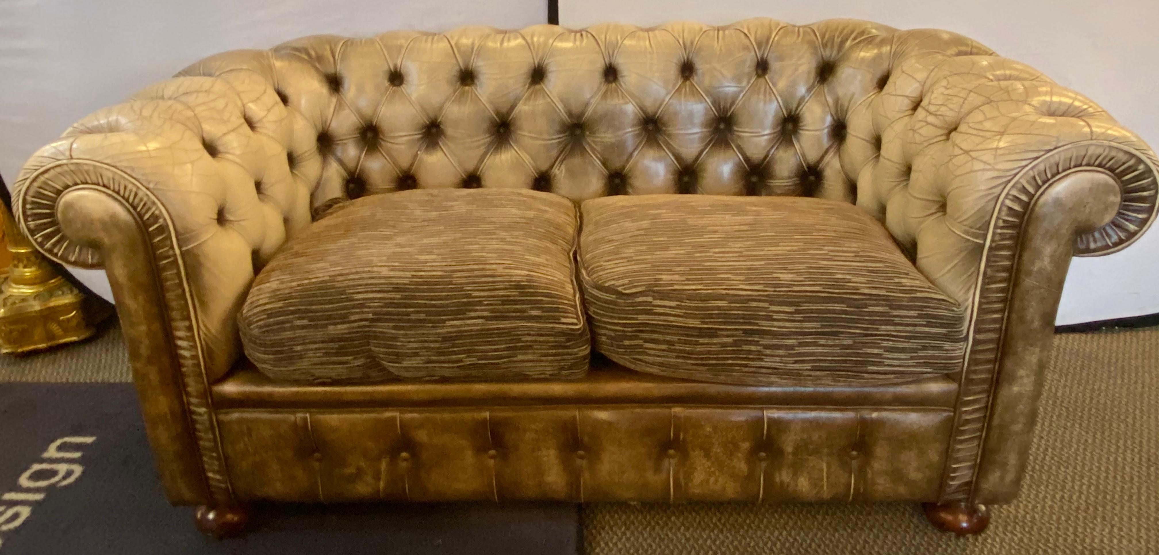 Chesterfield leather upholstered loveseat Sofa. This more than likely English Chesterfield has bun feet supporting a worn leather frame. The cushions are done in a designer fabric.
ELS.
