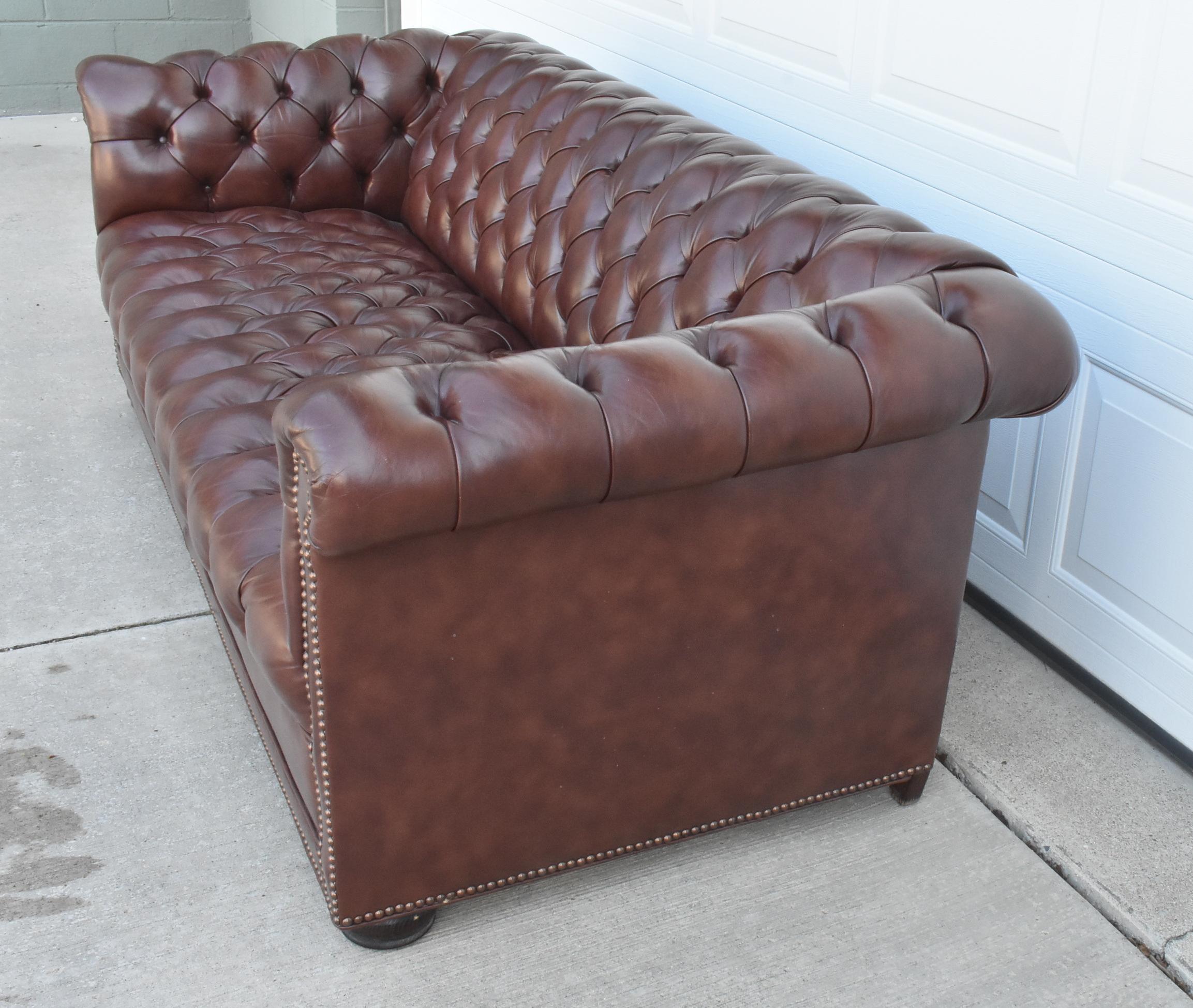 Gorgeous chesterfield in rich brown leather by Classic Leather Co circa 1980's. This sofa features thick brown leather, brass nail head trim, and heavy solid construction. 76
