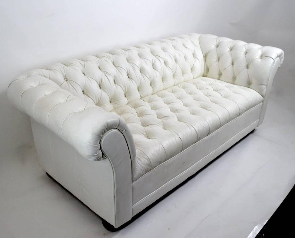 Chic and stylish tufted white vinyl Chesterfield loveseat sofa on wood bun feet. Overall excellent condition, showing only light wear to fronts of armrests, as pictured. Clean, original, ready to use condition, seat H 17.5 inches.