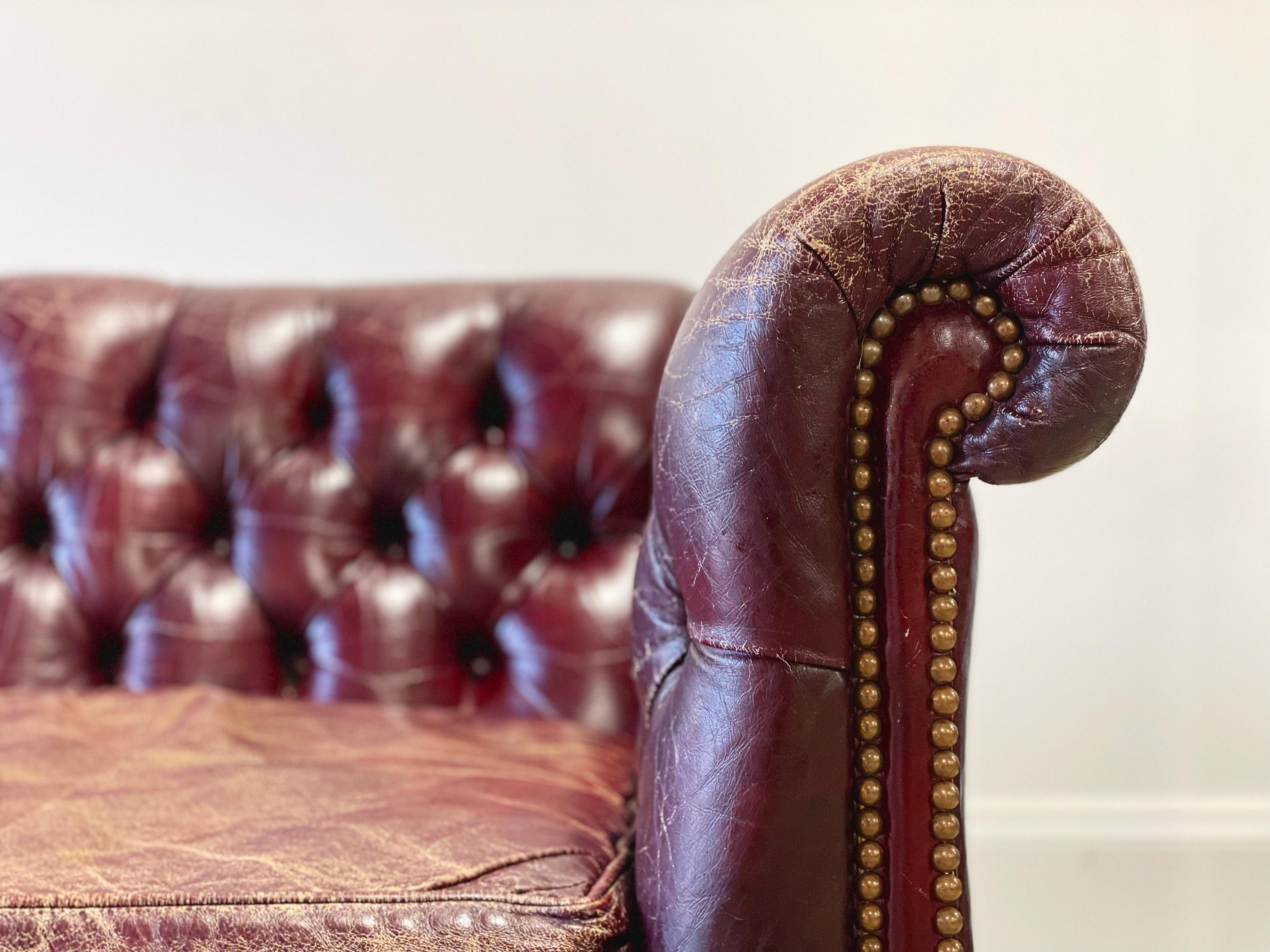 Vintage English Georgian style chesterfield sofa or settee in perfectly worn ox blood tone leather and solid sculpted mahogany frame. The frame is case shaped with rolled arms and decorative brass nail heads. Excellent joinery and craftsmanship with