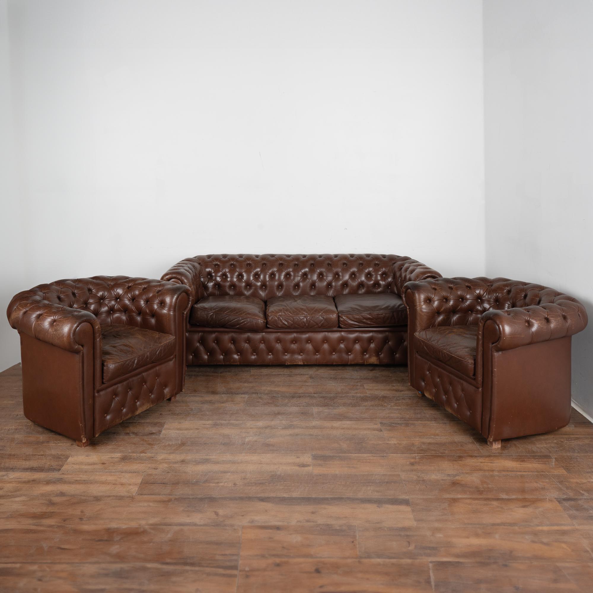 Set (3) vintage leather Chesterfield style sofa and pair of club arm chairs.
The brown leather has traditional tufted buttoned accents and rolled arms, hard wood block feet.
Sold in used vintage condition.
Mulitiple scuffs, scratches, impressions,