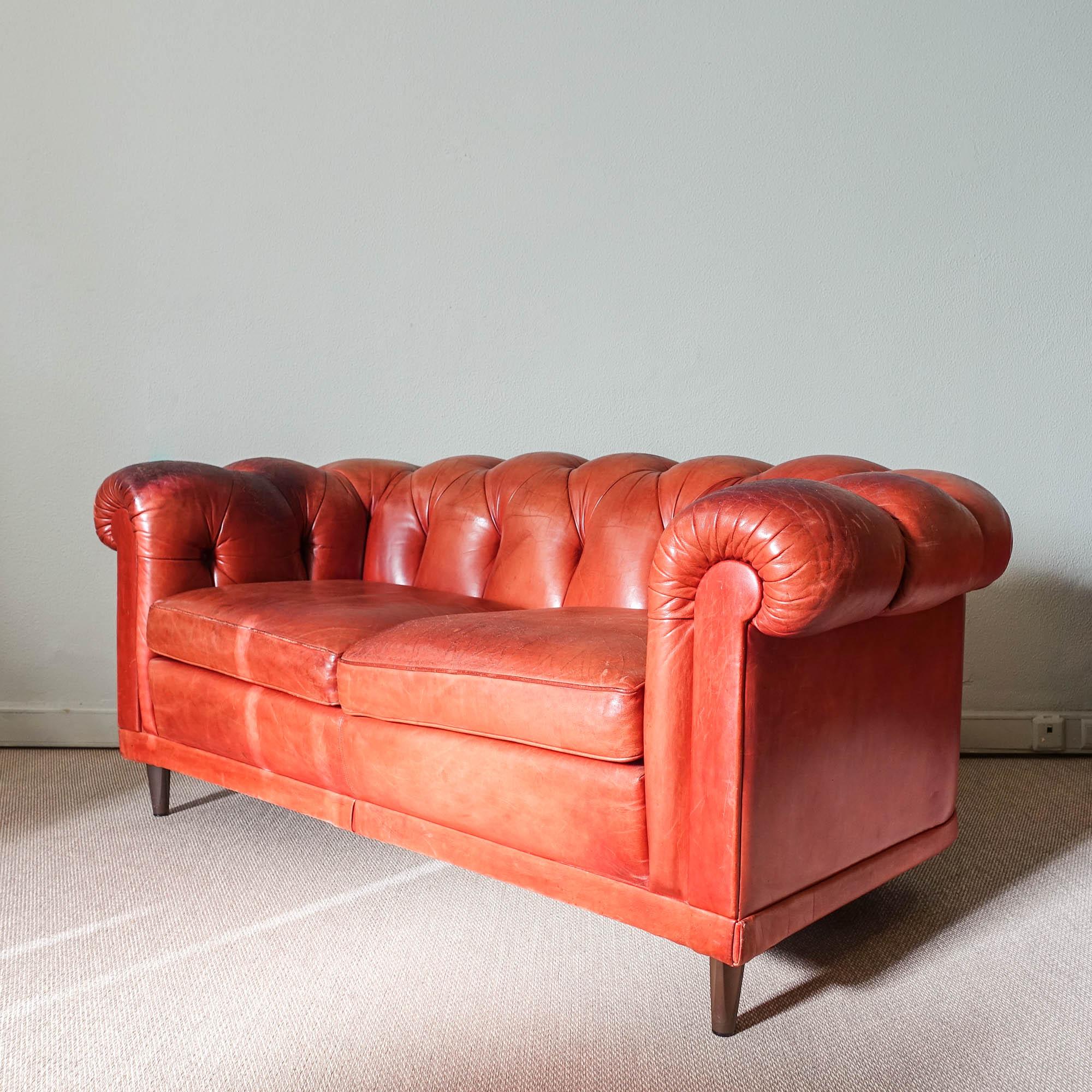 This two-seater leather sofa in Chesterfield style was designed and produced by Hans Kaufeld, in Germany, during the 1970's. It features a heavy wooden frame construction, upholstered and covered with brown leather. Tufted back and armrests. Loose