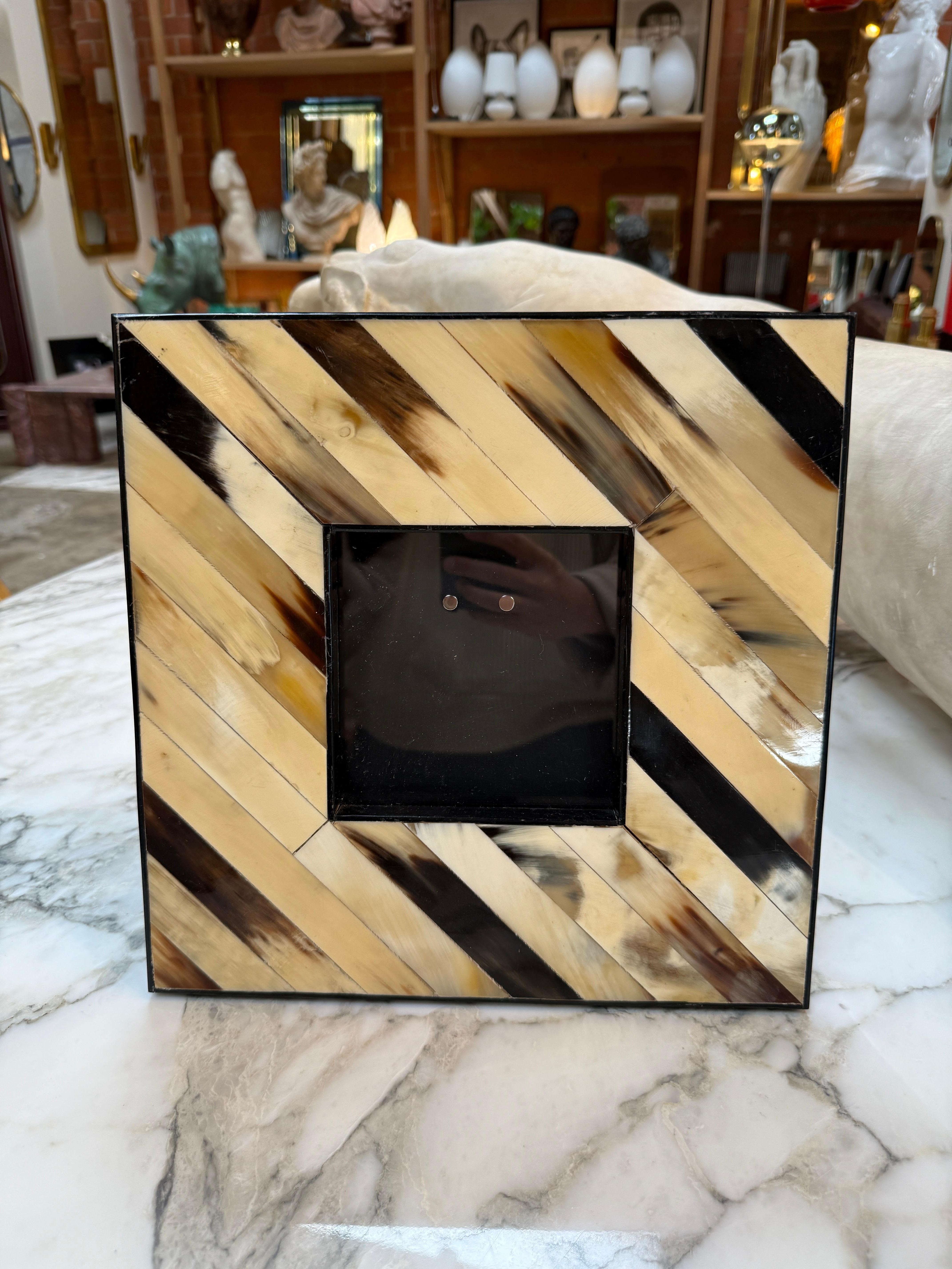 Ce cadre photo carré de fabrication artisanale présente une incrustation de chevrons audacieux en corne naturelle polie à la main. L'alternance de tons clairs et foncés de la corne - allant de l'ivoire doux à l'espresso profond - crée un motif