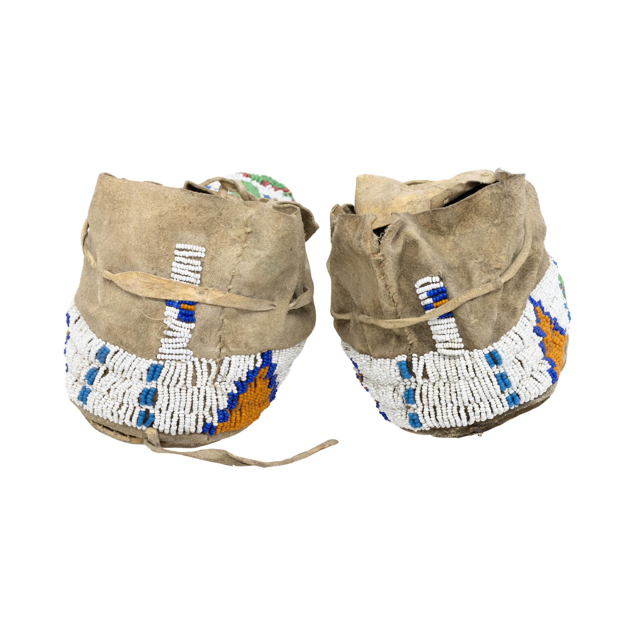 Pair of Cheyenne beaded moccasins with buffalo hoof motif. Sinew sewn. With colors of green, orange, blue, and white. Right moccasin has water damage to the sole from in period use, and upper is a little stiff. Circa 1890. 11