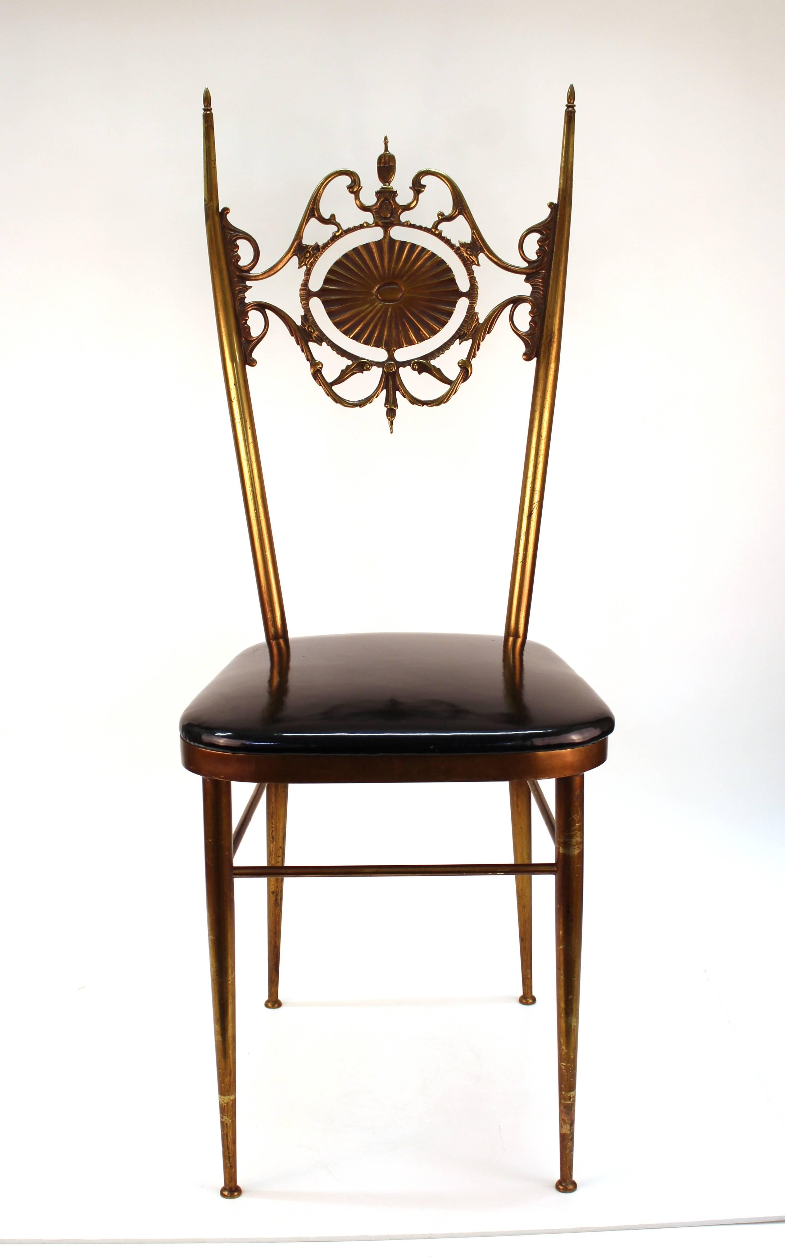 Chiavari side chair crafted in brass with black patent seat and elaborate splat. Features thin elongated back and legs. The ornate back includes scroll work and a sun disk with a relief depicting the myth of Leda and the Swan on the reverse. The