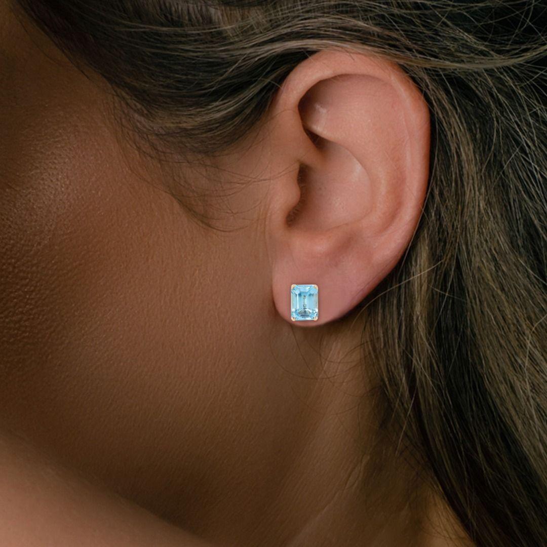 Indulge in the vibrant allure of these chic 14K yellow gold stud earrings, featuring two mesmerizing emerald-cut blue topaz stones. The main stones, with a combined carat weight of 3.00ct, exhibit a brilliant blue hue that instantly captivates the