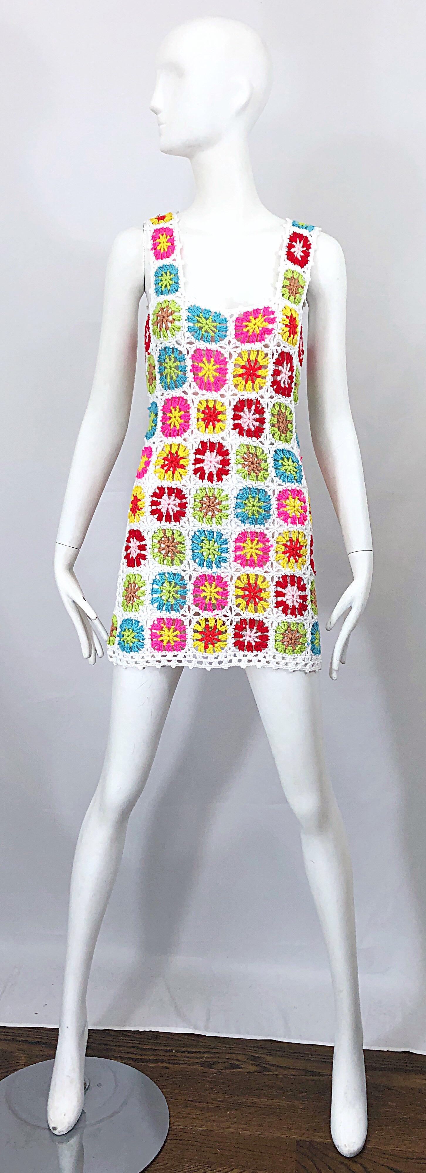 Chic late 1960s hand crochet colorful flower power mini dress or tunic top! Features a white backdrop with vibrant colors of hot pink, pink, yellow, green, turquoise blue and orange throughout the front and back. Simply slips over the head and