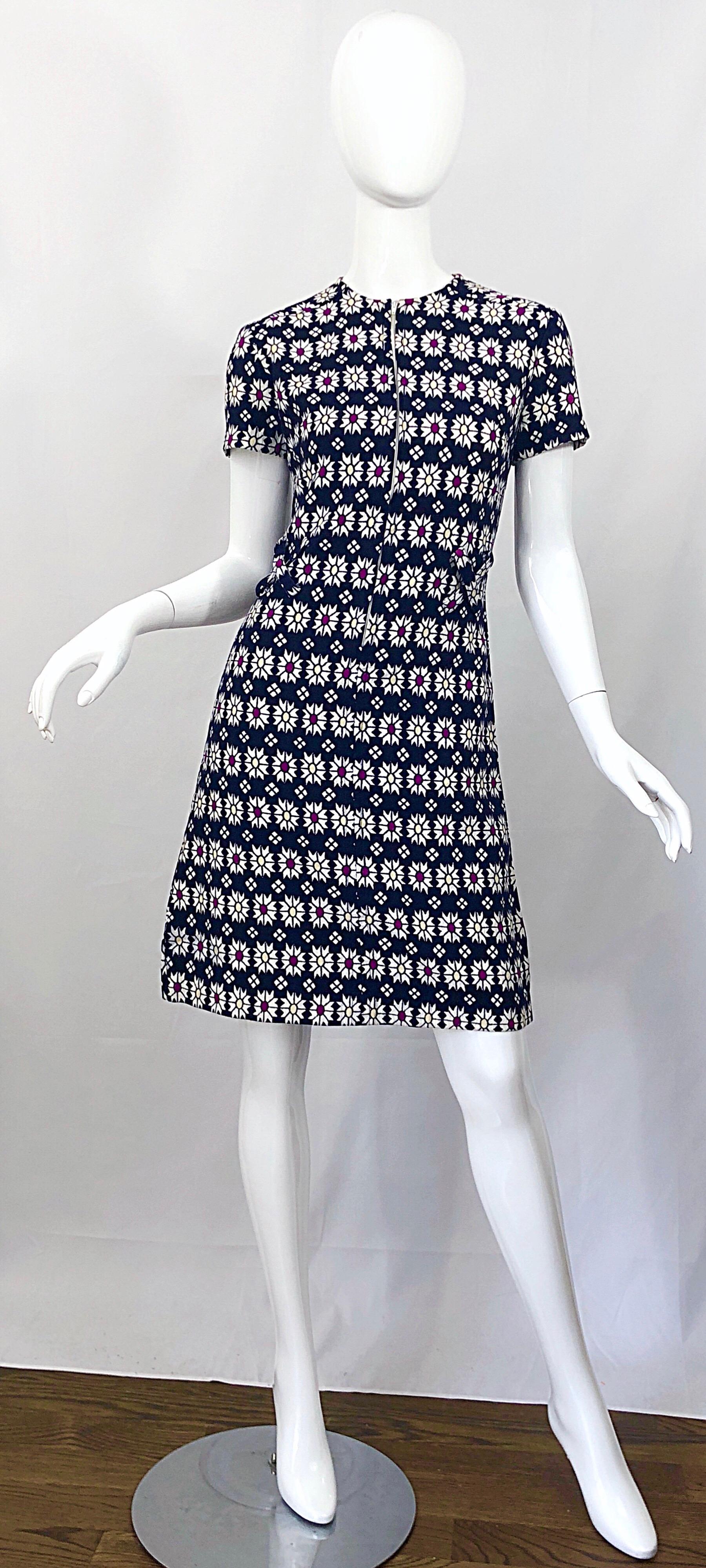 Super chic mid 1960s navy blue, fuchsia purple and yellow geometric daisy print A - Line dress! Features a fitted bodice with a flattering A-Line skirt. Criss-cross strap details at each side on the front and back. POCKET at the side of the hip.