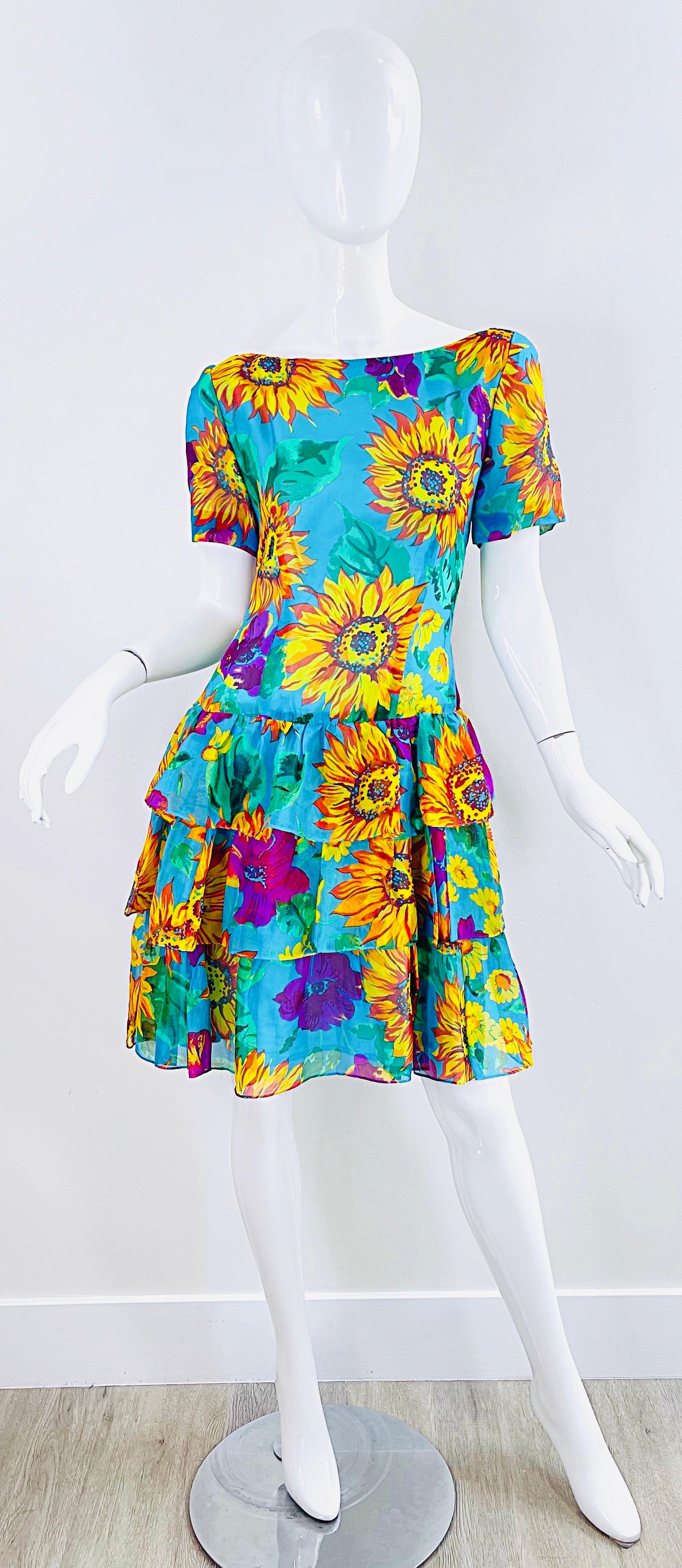 Schickes kurzärmeliges Kleid aus Seidenchiffon mit Sonnenblumen- und Hibiskusdruck aus den späten 80ern ! Mit tailliertem Mieder und abgestuftem Rüschenrock. Verdeckter Reißverschluss auf der Rückseite mit Haken- und Ösenverschluss. 
Toll mit Gürtel