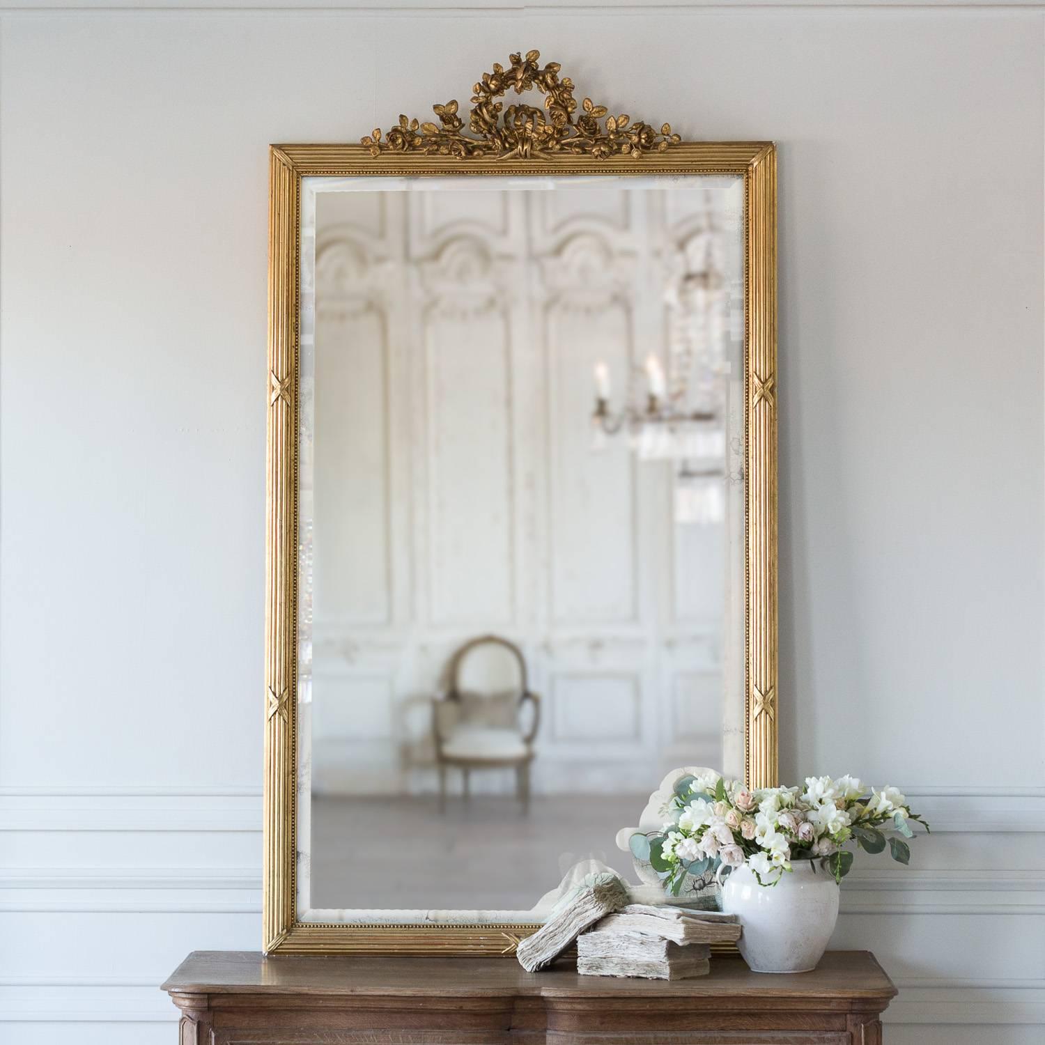 Bevelled glass mirror with a large, elaborate crest. A sweet rose motif crowns the top of this otherwise simple mirror. Bows on the frame break up the long lines of column design. The original, bevelled mercury glass shows a significant amount of