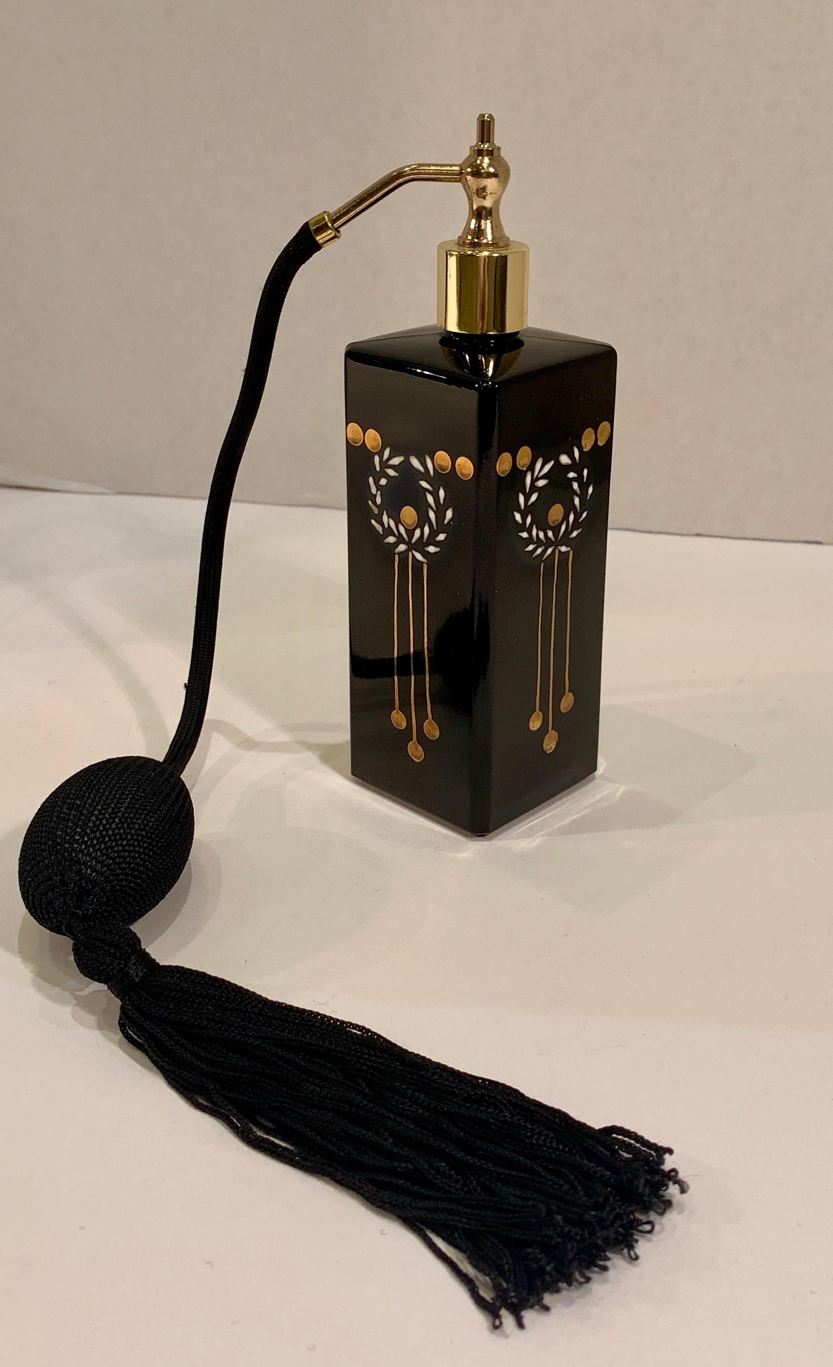 Chic, Hollywood Regency inspired, black glass perfume bottle with black atomizer and tassel features an unusual shape, square with cut corners, and a gold metal top. All four sides are hand painted in 24 karat gold and white with a laurel wreath