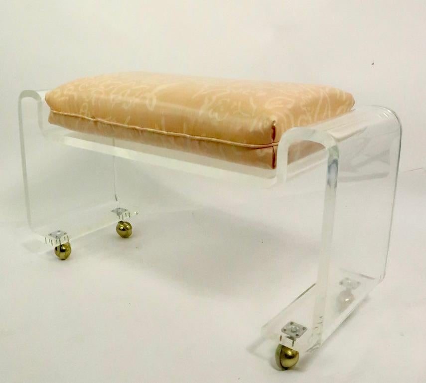 Chic and stylish solid Lucite bench, vanity stool, ottoman, having a loose cushion seat and ball coaster feet. This example is in very fine, original condition, clean and ready to use. In the style of Charles Hollis Jones, unsigned. Lucite. 75 inch