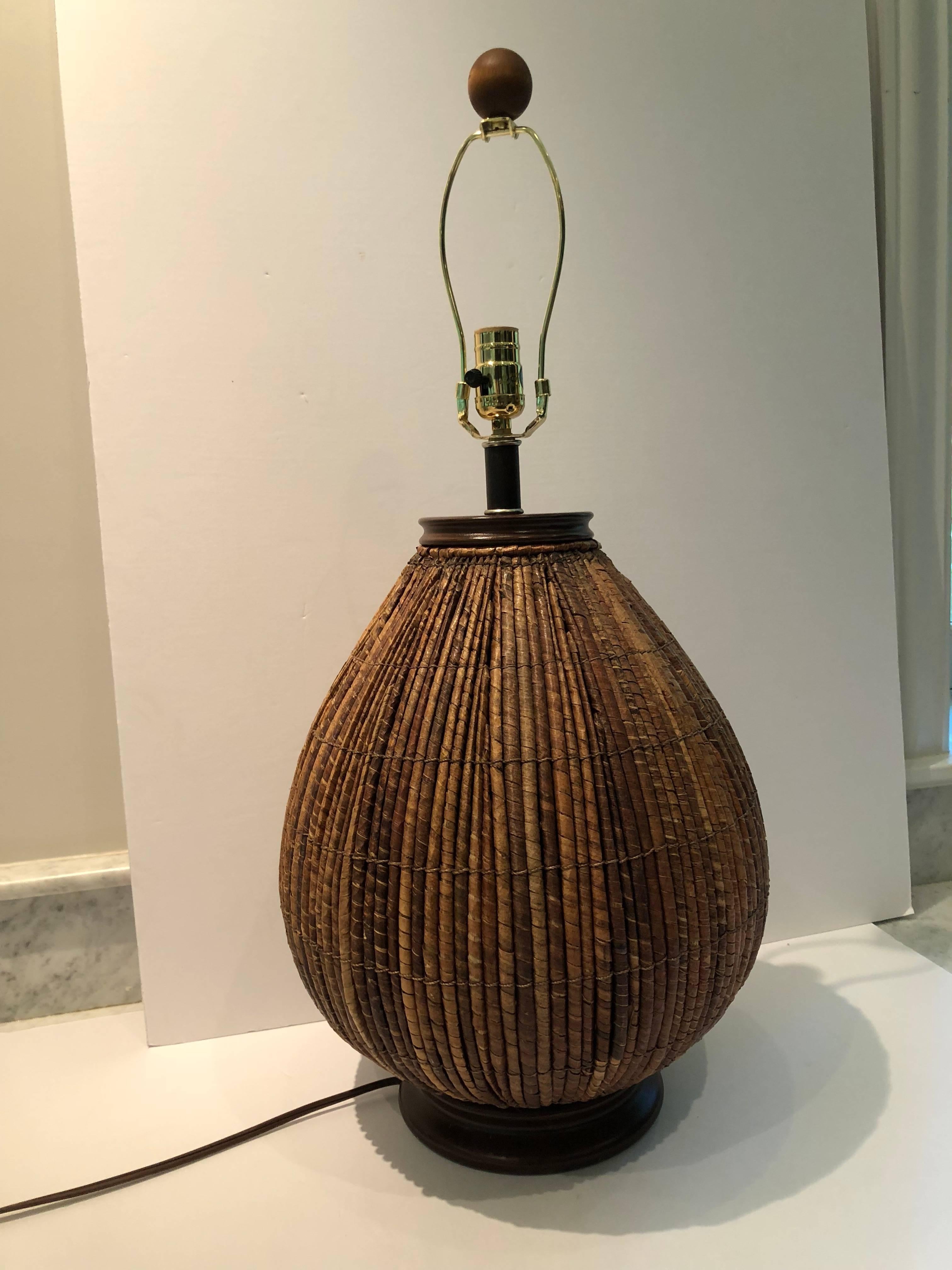 Large midcentury rattan lamp by Palecek. The lamp has a dark wooden base and neck and round finial. The rattan is of varying shades of brown adding to it’s textural appeal. . Custom shade in off-white linen lined in taupe silk.
 