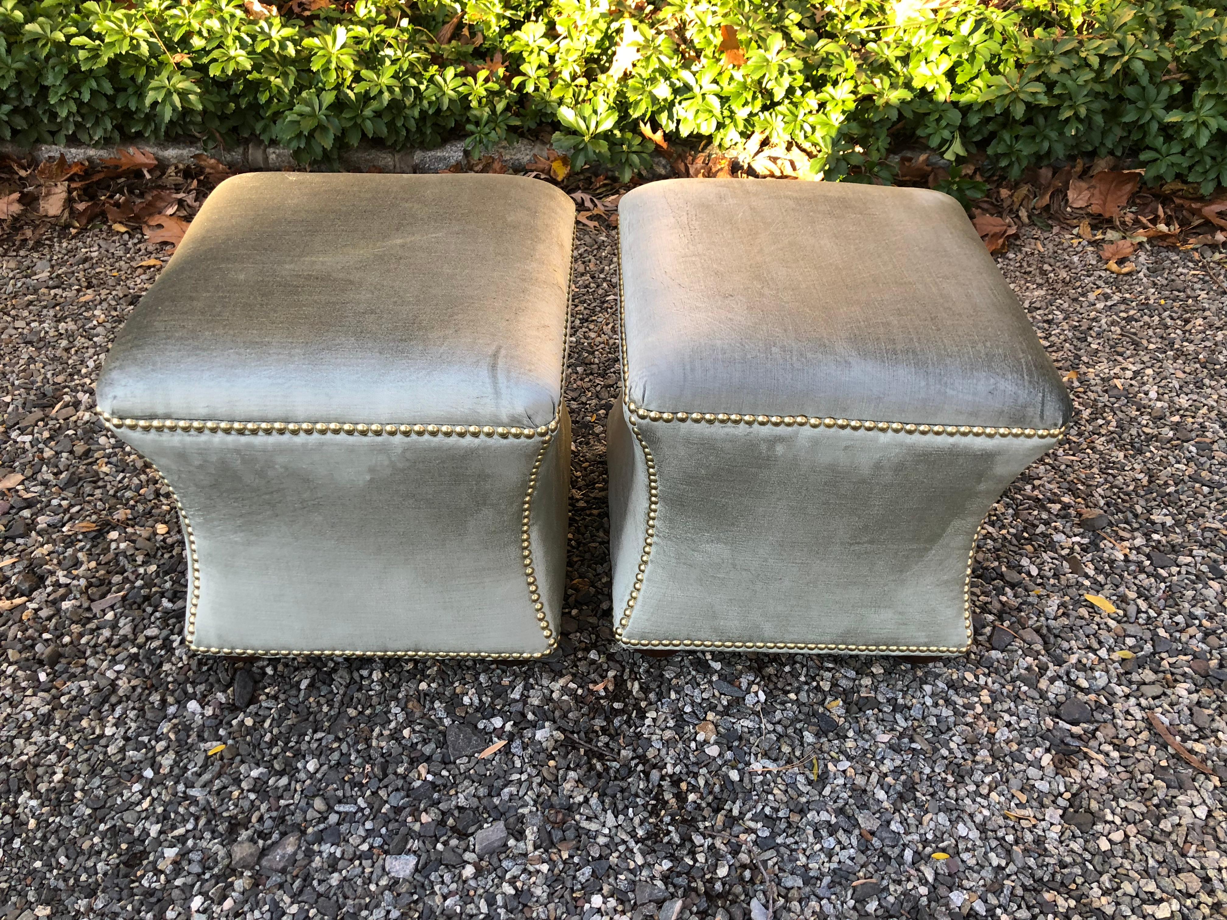 Sophisticated pair of hour glass shaped ottomans in grey green silk velvet. French brass nailhead trim and wooden bun feet. Made by Duralee.