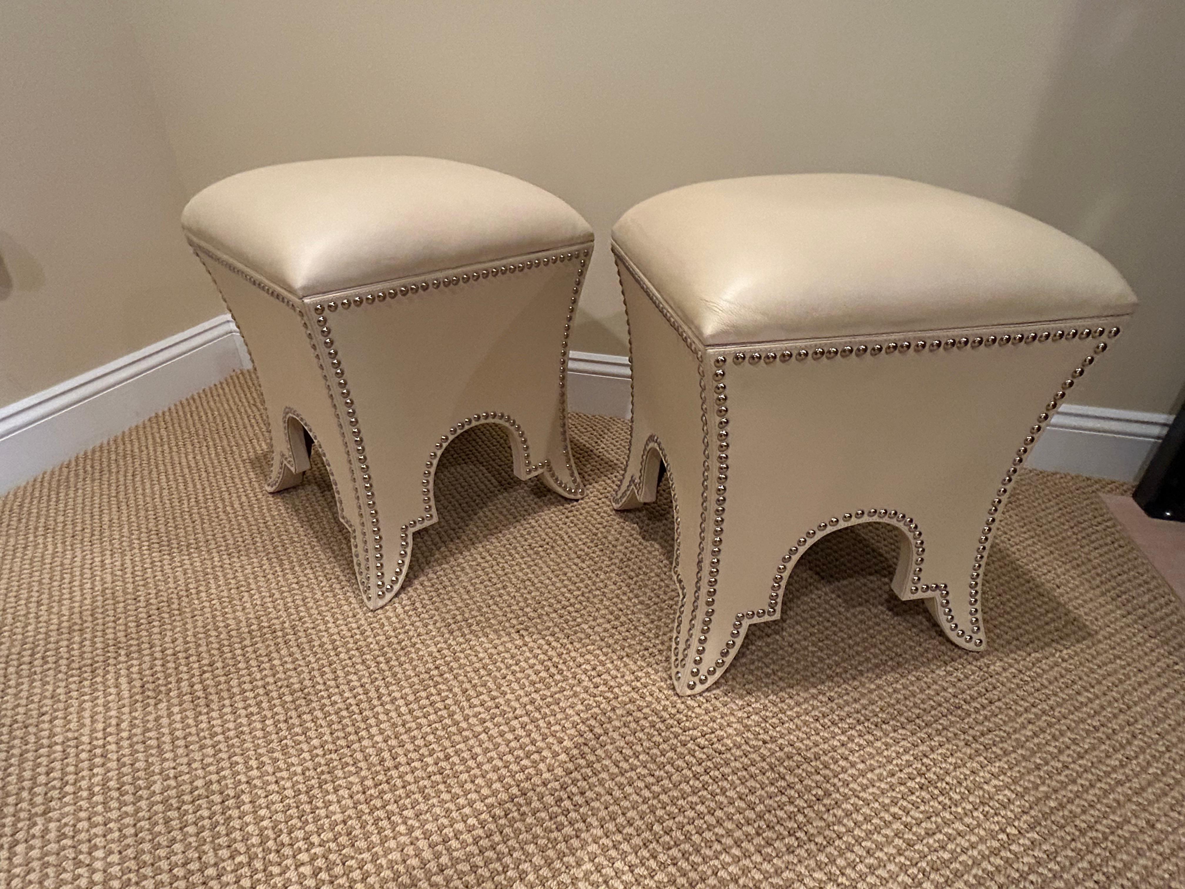 Elegante coppia di pouf imbottiti in ecopelle color crema che si aprono per rivelare un contenitore all'interno.  Rifinite con teste di chiodi argentate e con basi sagomate di grande fascino.