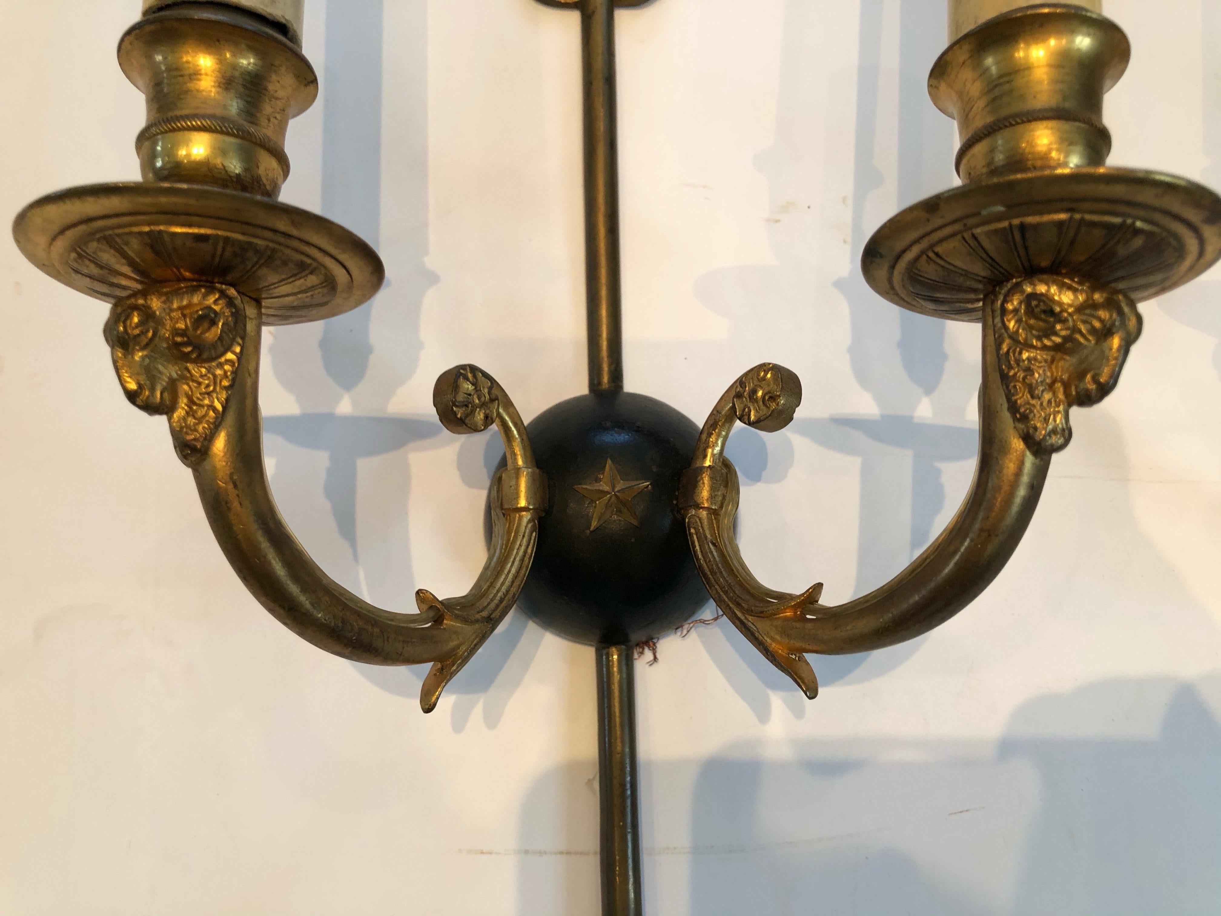 Pair of brass and ebonized Regency style wall sconces having an arrow motif and rams heads at the base of each light; the center sphere is black with a brass star.
