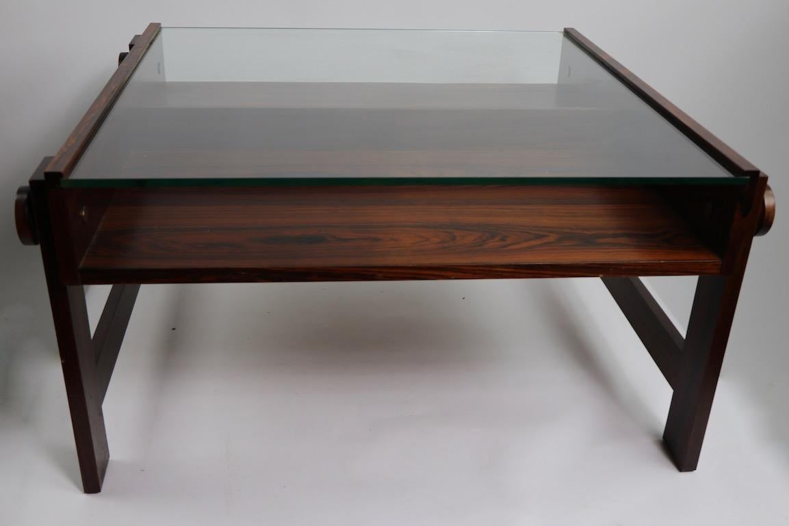 Architectural design, chic and stylish coffee table having a rosewood structure with thick plate glass top surface. Probably Brazilian in origine, however the table is unsigned. 3.5 inch opening between glass top and rosewood shelf.
Originally