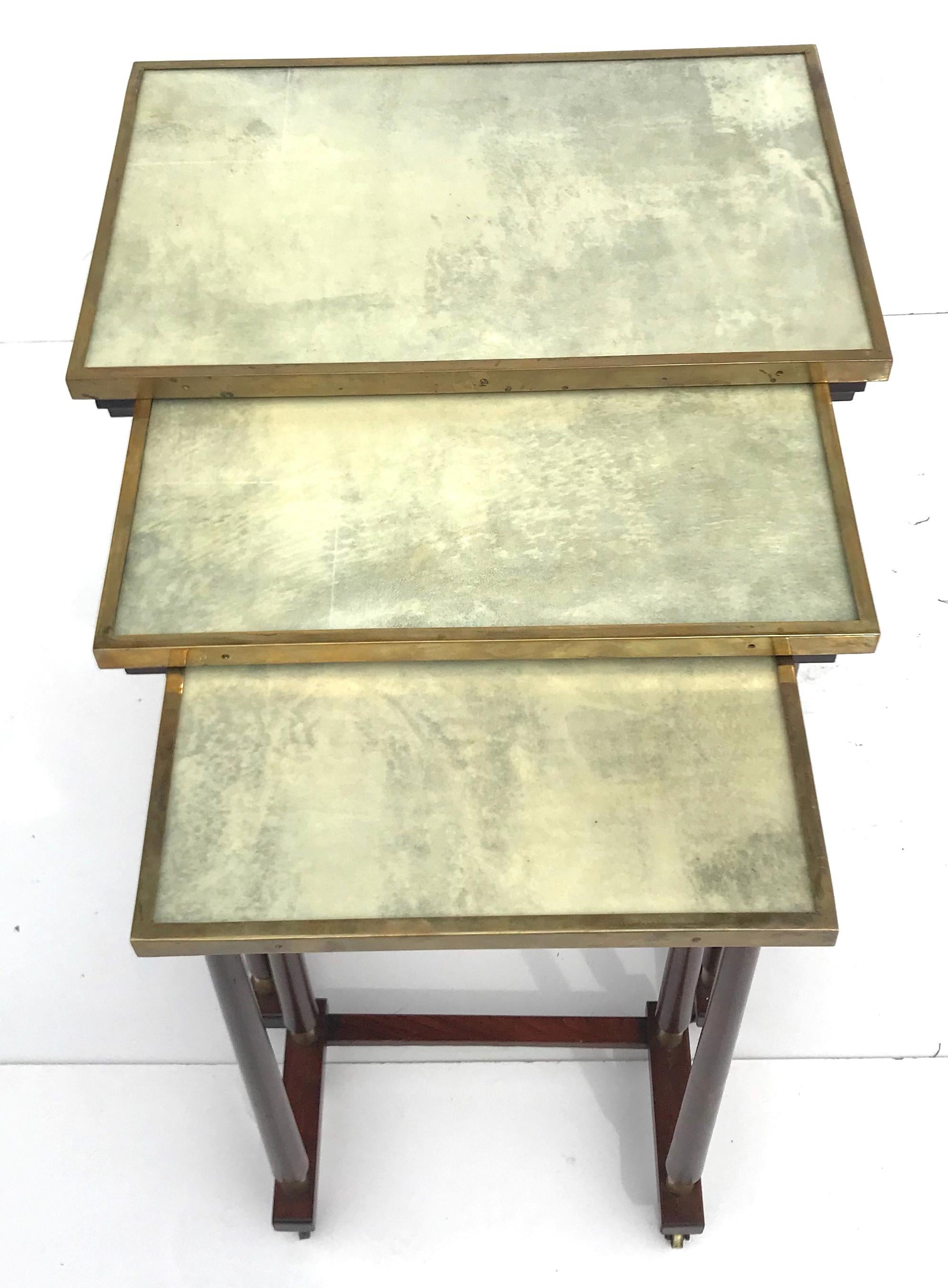 Chic set of 1950s Italian modern nesting tables in the style of Paolo Buffa. Intricately designed, and beautifully crafted, they feature inlaid brass-framed parchment tops under glass, and mahogany legs with brass details and castors. Truly a