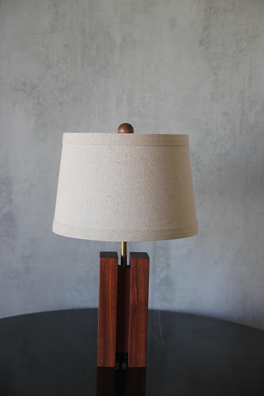 A beautifully crafted sculptural Mahogany reddish-brown blocks form a table lamp having 3 in square cube-shaped wooden, columns height (outside column 9 in, inside column 7 in) with organic, clean, and sophisticated design (Brass - Wood and Linen