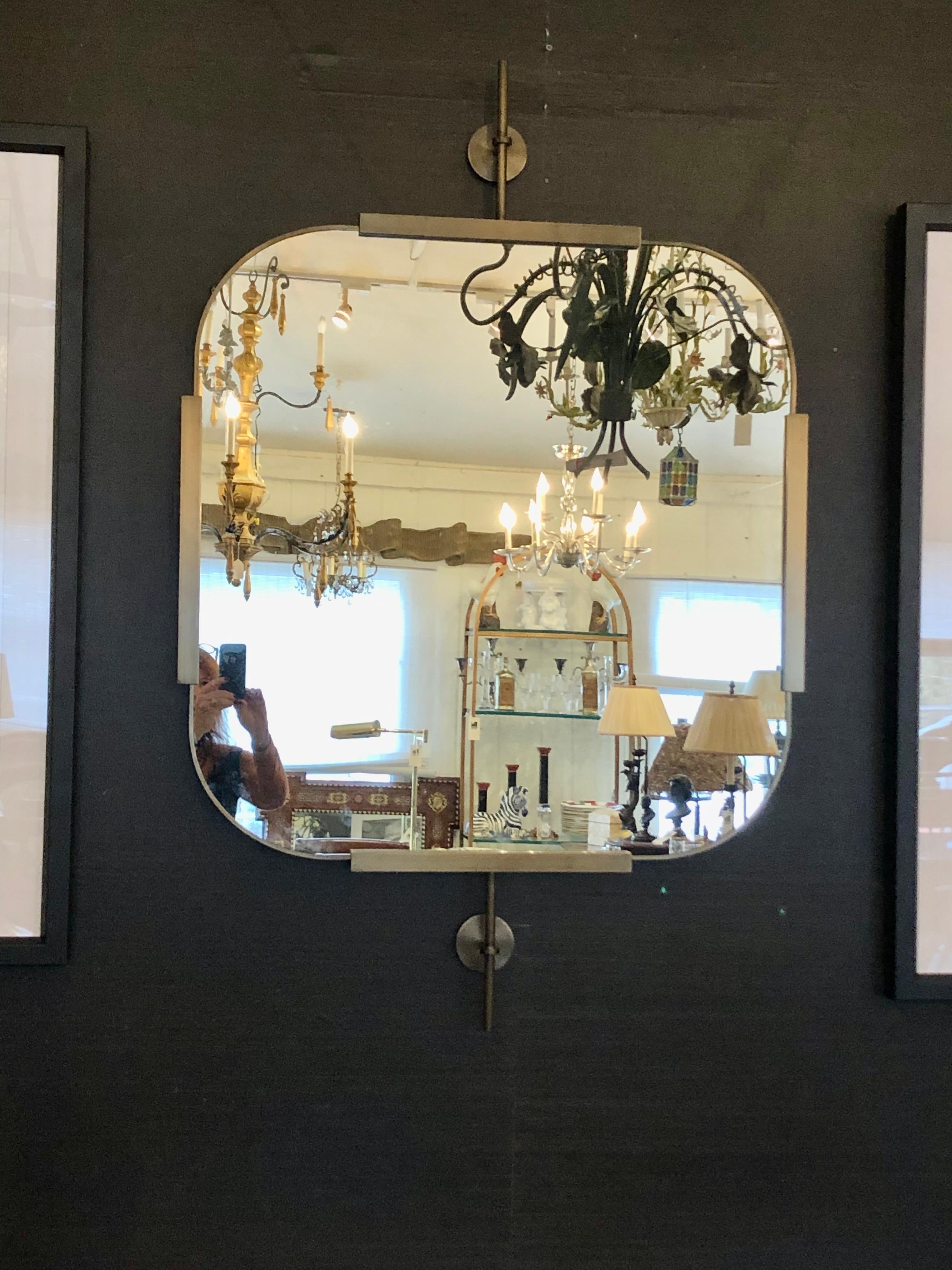 Sophisticated contemporary brushed brass almost square mirror that seems to float away from the wall, having two industrial inspired finials at top and bottom. 
 There is a french cleat for hanging, and mirror actually does hang with space behind