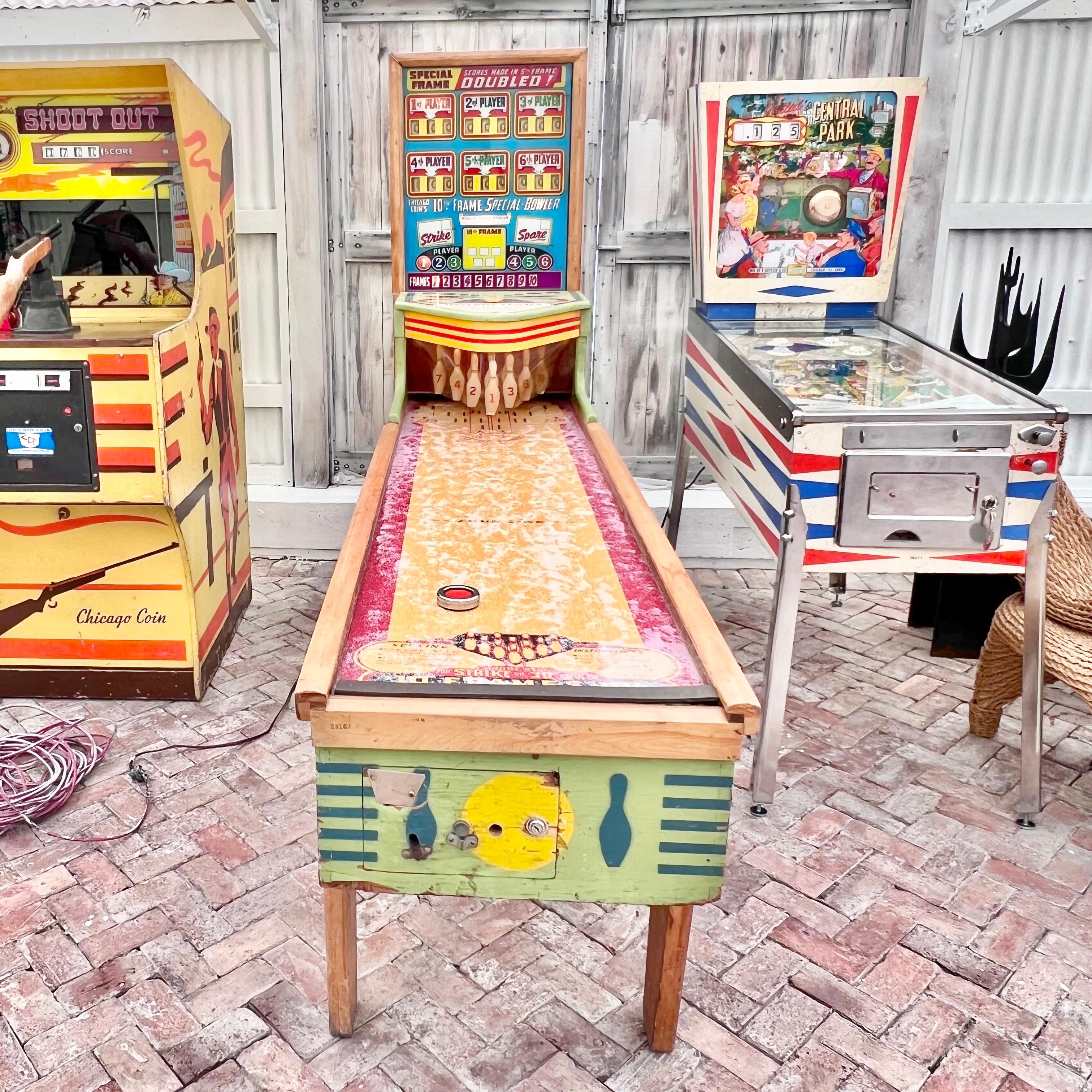 Vintage bowling arcade machine from 1949 manufactured by Chicago Coin. Wooden cabinet painted with bowling designs in primary colors, lighted scoreboard and Formica lane. Player uses shuffle board style puck to hit pins. Up to 6 players can play